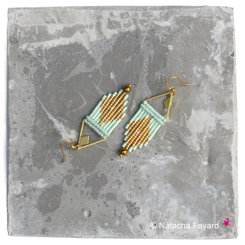 Peut inclure: Une paire de boucles d'oreilles géométriques dorées et vert clair avec un design triangulaire. Les boucles d'oreilles sont faites de petites perles et sont suspendues à des crochets dorés.