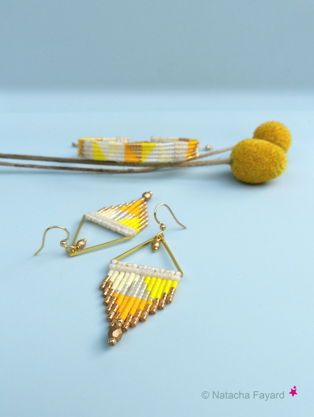 Peut inclure: Un ensemble de boucles d'oreilles et un bracelet assortis en perles jaunes, blanches et dorées. Les boucles d'oreilles sont de forme triangulaire et pendent à des crochets dorés. Le bracelet est une simple bande avec un motif géométrique.