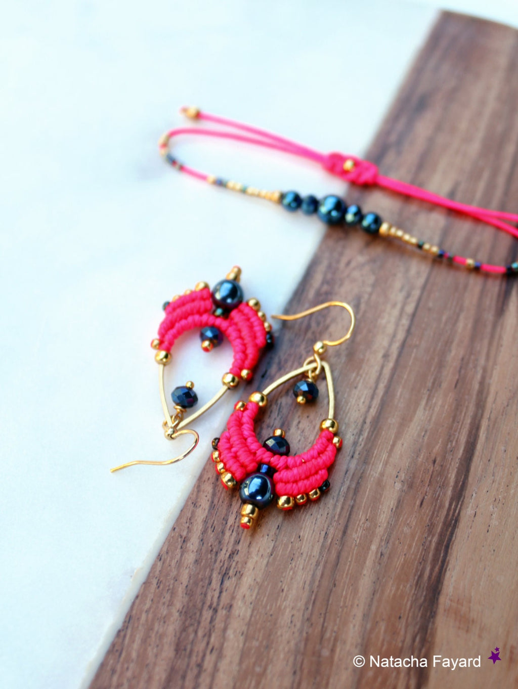 Peut inclure: Une paire de boucles d'oreilles rose et or avec des perles noires. Les boucles d'oreilles sont réalisées à l'aide d'une technique de macramé et ont une forme de goutte.