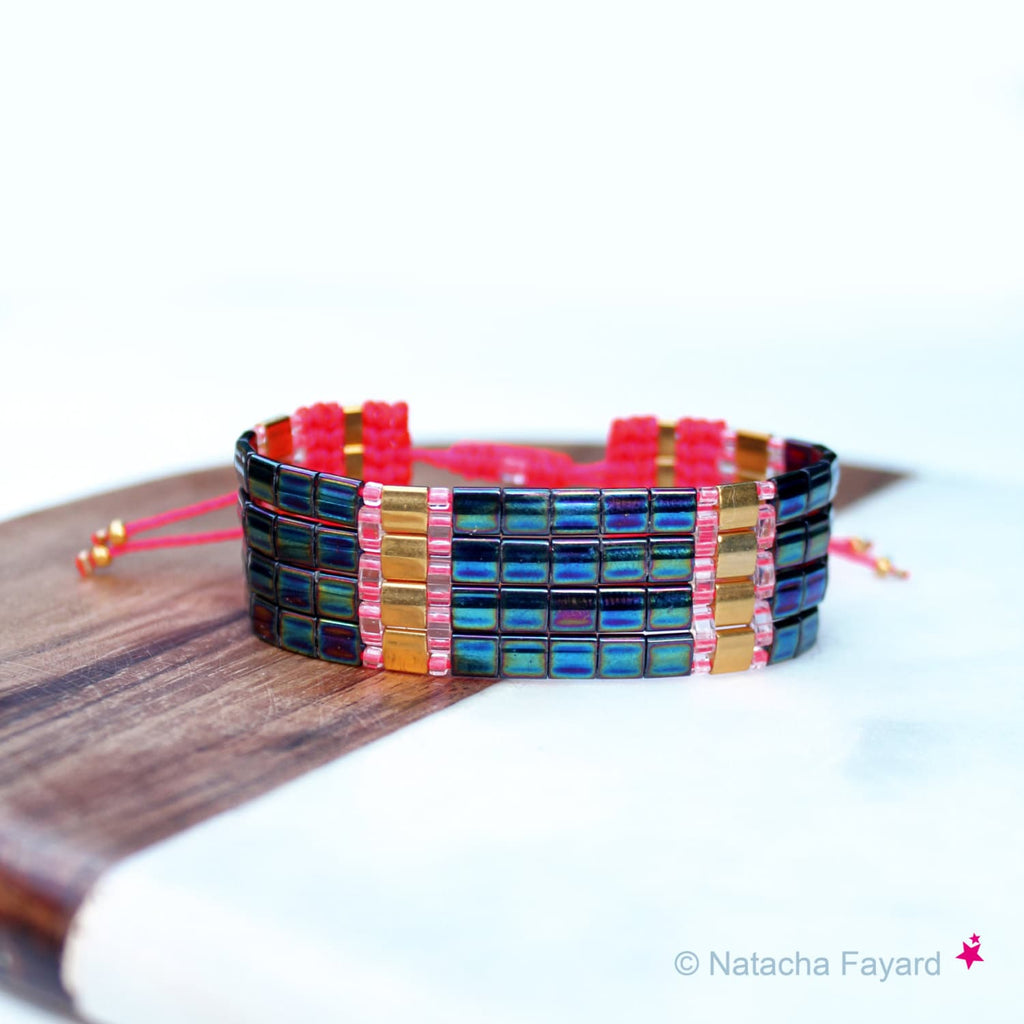 Peut inclure: Un bracelet multi-rangs avec des perles carrées bleu et vert irisées, des perles dorées et du fil rose.