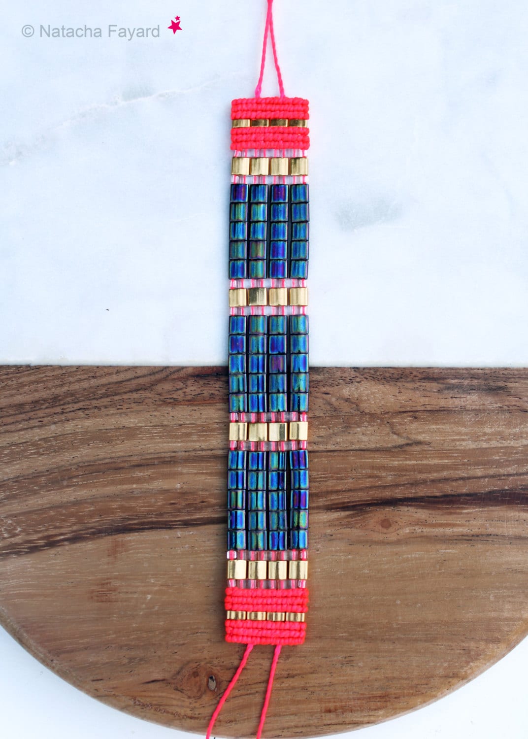 Peut inclure: Un bracelet multi-colore en perles bleues, dorées et roses. Le bracelet est composé de perles carrées et est doté d'un cordon de fermeture rose.
