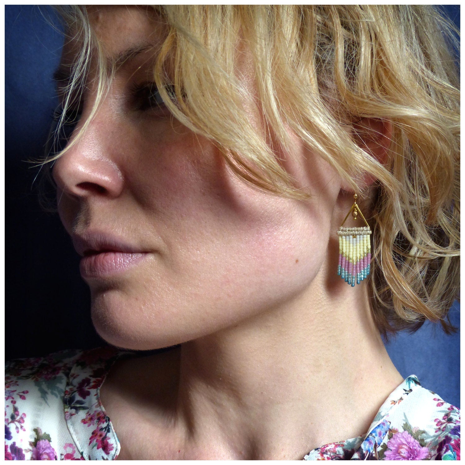 Peut inclure: Une femme aux cheveux blonds portant une paire de boucles d'oreilles en perles dorées et multicolores. Les boucles d'oreilles sont de forme triangulaire et présentent un dégradé de perles roses, jaunes et bleues.
