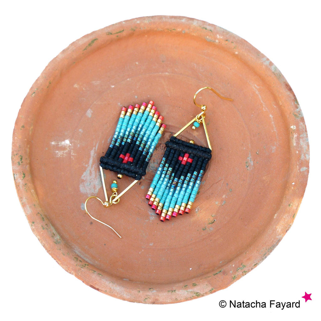 Peut inclure: Une paire de boucles d'oreilles en perles turquoise et noires avec des accents dorés. Les boucles d'oreilles sont en forme de triangle et ont un motif de croix rouge.
