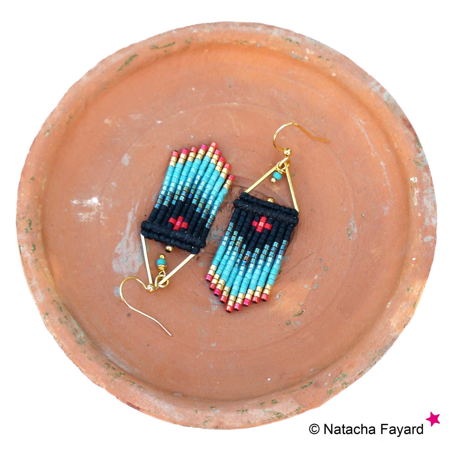 Peut inclure: Une paire de boucles d'oreilles en perles turquoise et noires avec des accents dorés. Les boucles d'oreilles sont en forme de triangle et ont un motif de croix rouge.