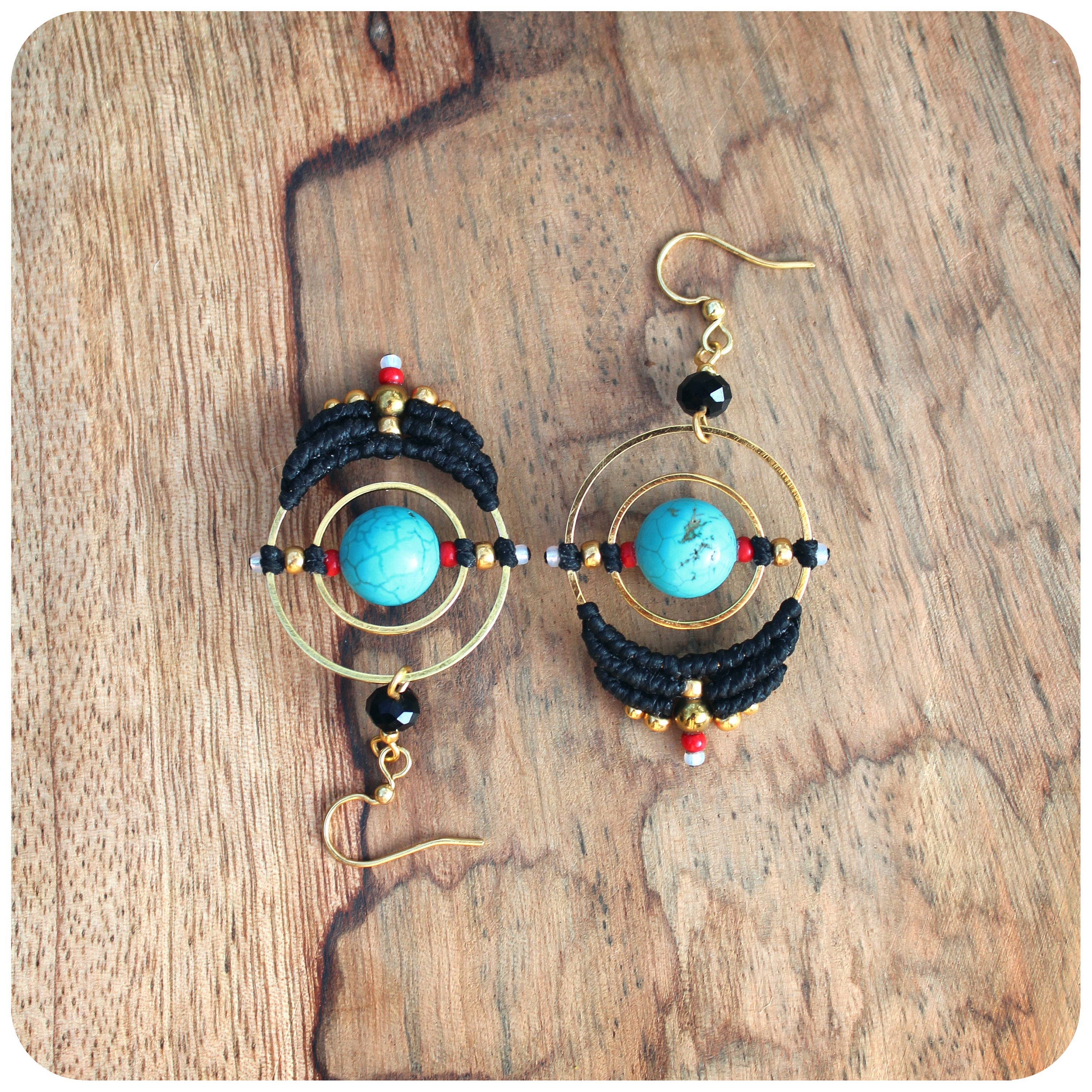 Peut inclure: Une paire de boucles d'oreilles créoles dorées avec du macramé noir et des pierres turquoise. Les boucles d'oreilles ont un design géométrique avec un cercle et un cercle plus petit à l'intérieur.