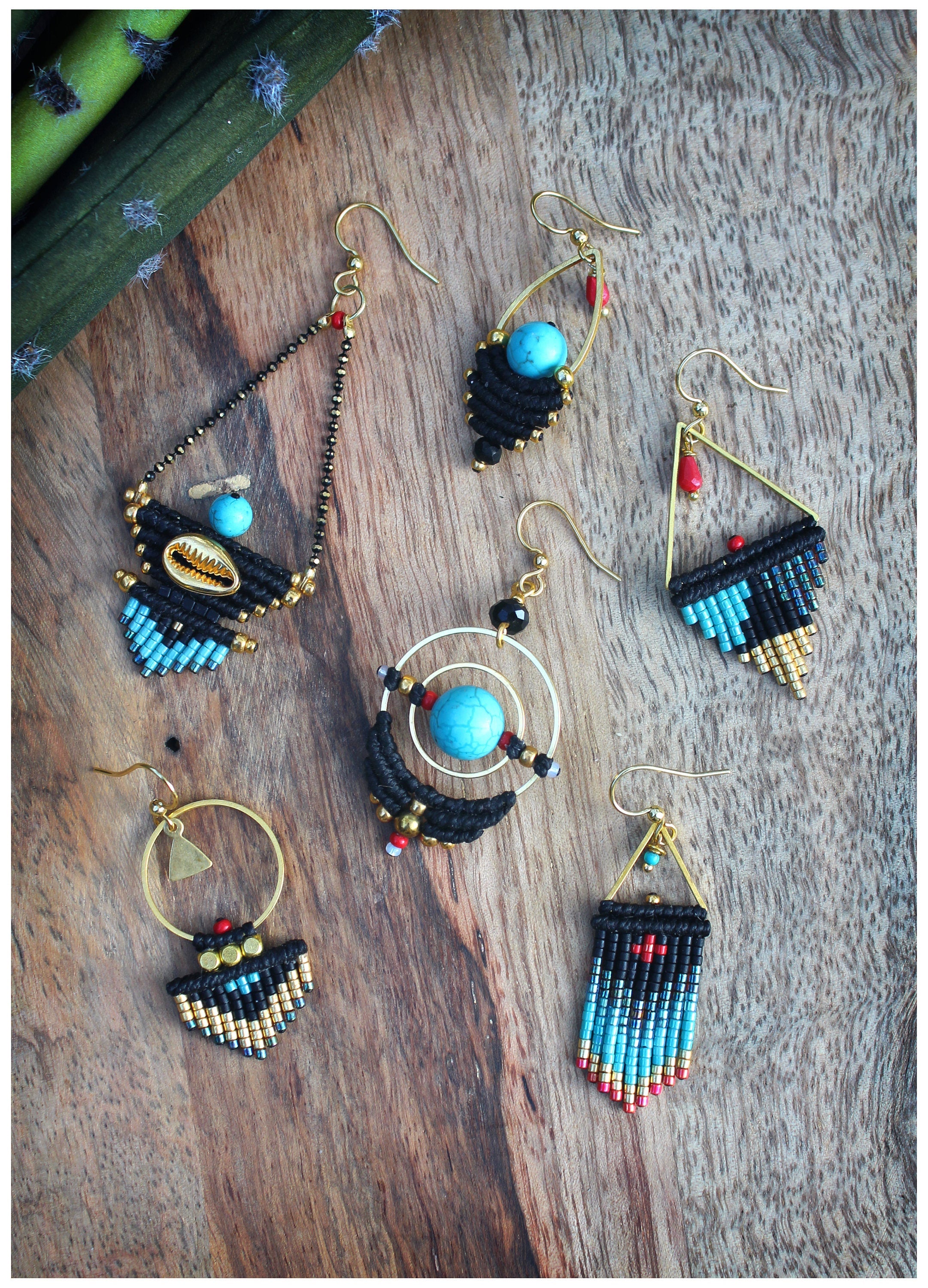 Peut inclure: Cinq paires de boucles d'oreilles faites à la main avec des accents noirs et dorés. Chaque paire présente un design différent avec des perles turquoise et rouges.
