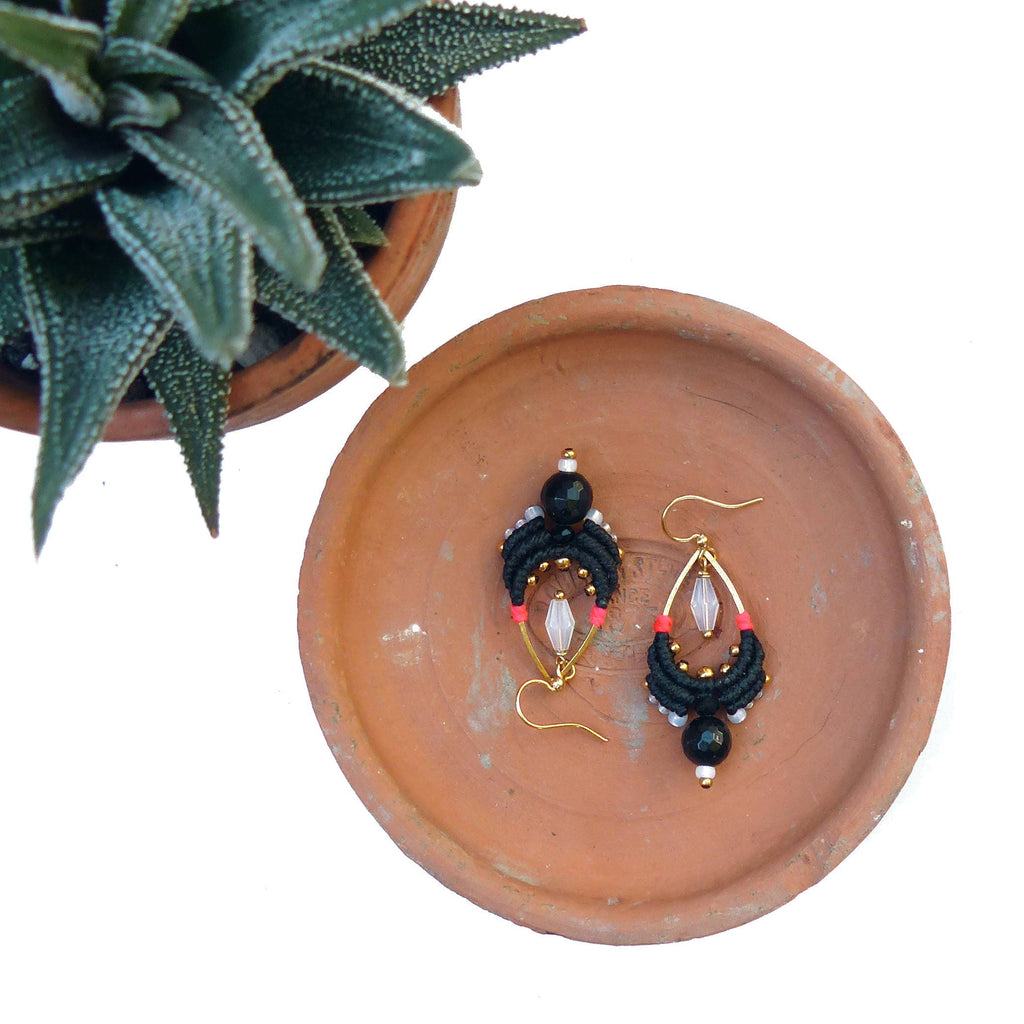 Peut inclure: Une paire de boucles d'oreilles noires et dorées avec un pendentif en cristal en forme de larme. Les boucles d'oreilles sont faites de fil noir et ont un design perlé.