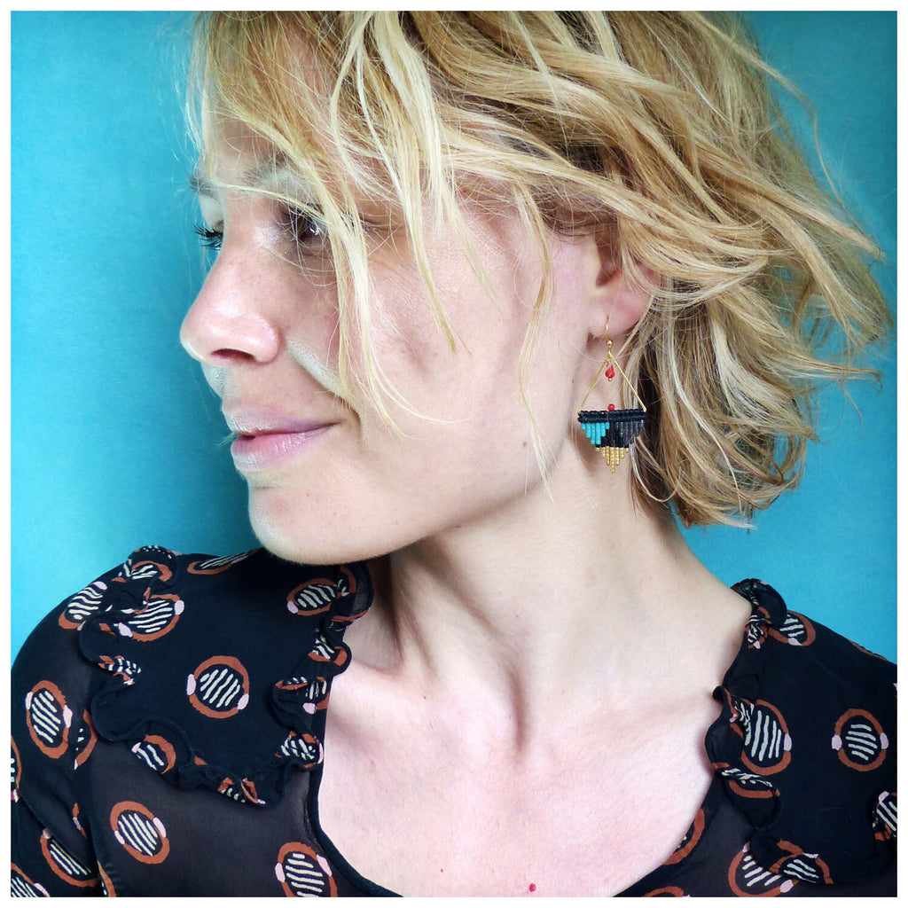 Peut inclure: Une femme aux cheveux blonds portant une chemise à motifs noir et blanc avec une paire de boucles d'oreilles géométriques noires, turquoise et dorées.