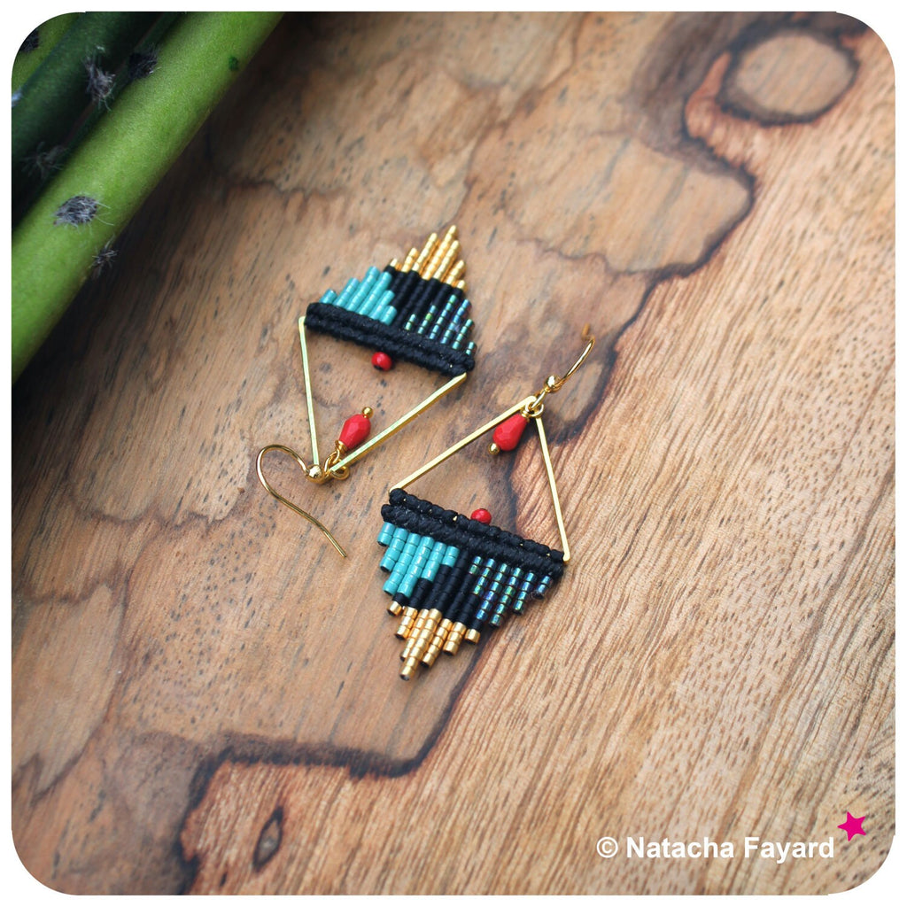 Peut inclure: Une paire de boucles d'oreilles triangulaires géométriques avec des perles noires, turquoise et dorées. Les boucles d'oreilles ont un accent de perle rouge et des crochets dorés.