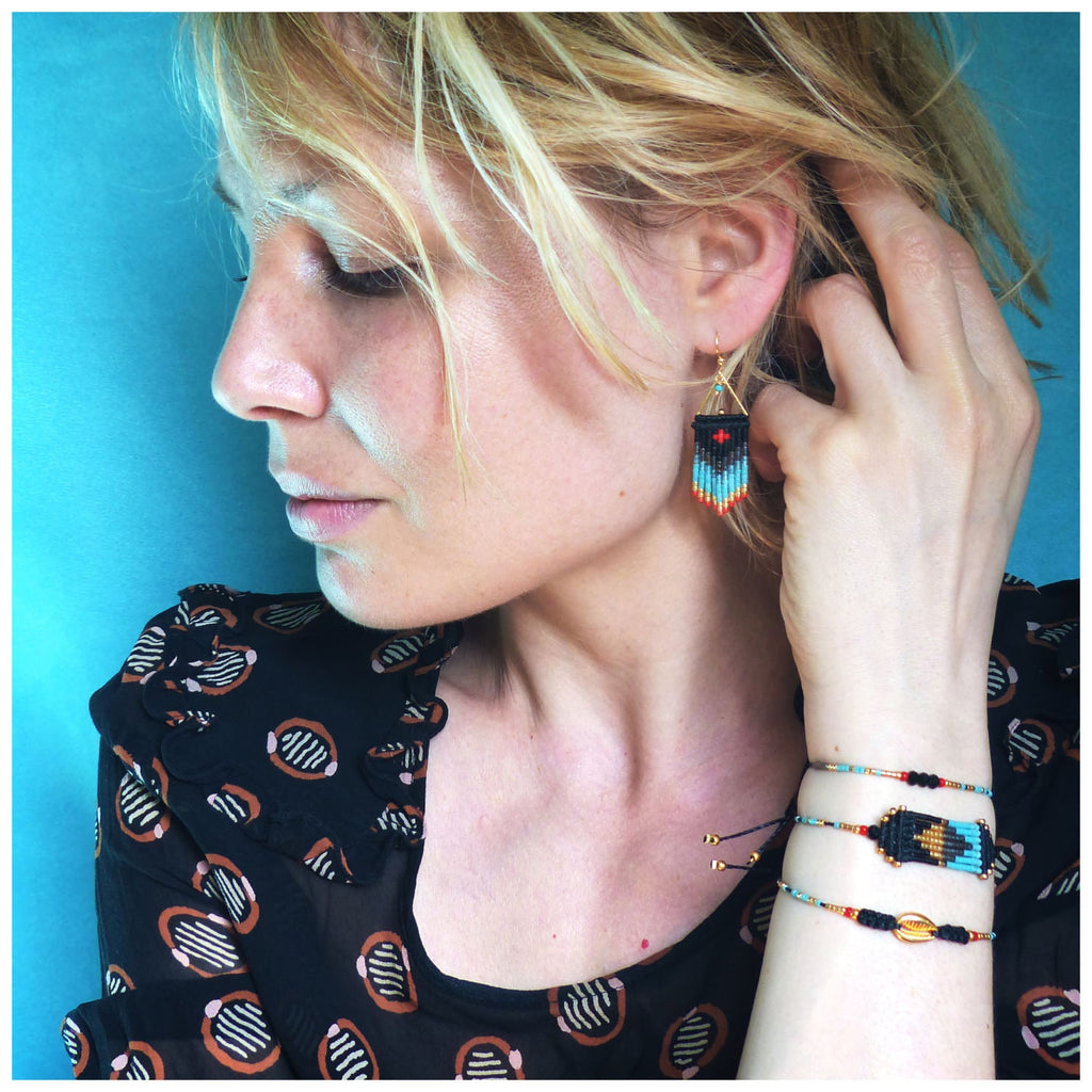 Peut inclure: Une femme portant un chemisier à motifs noirs et bruns avec des boucles d'oreilles et des bracelets en perles. Les boucles d'oreilles et les bracelets présentent des motifs géométriques en noir, turquoise et rouge.