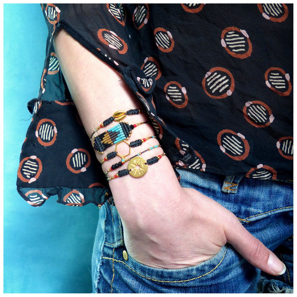 Peut inclure: Un ensemble de cinq bracelets avec des perles noires, rouges, bleues et dorées. Les bracelets présentent une variété de breloques, dont une étoile, un hexagone et une coquille. 