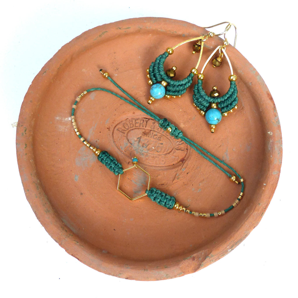 Peut inclure: Un ensemble de boucles d'oreilles en macramé vert et or et un bracelet avec des perles turquoise. Les bijoux sont présentés sur une assiette en terre cuite.