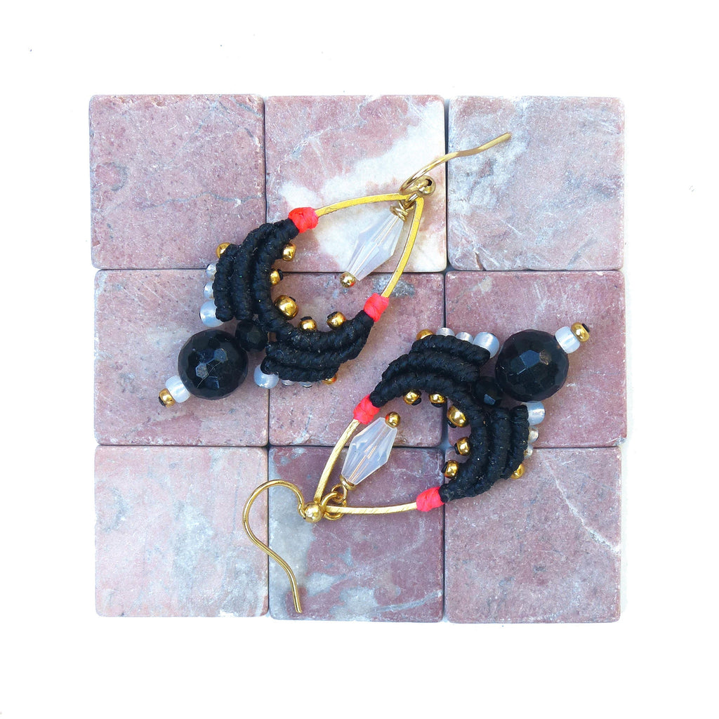 Peut inclure: Une paire de boucles d'oreilles noires et dorées en forme de larme. Les boucles d'oreilles sont faites de fil noir, de perles dorées et de cristaux transparents. Les boucles d'oreilles sont suspendues à des crochets dorés.