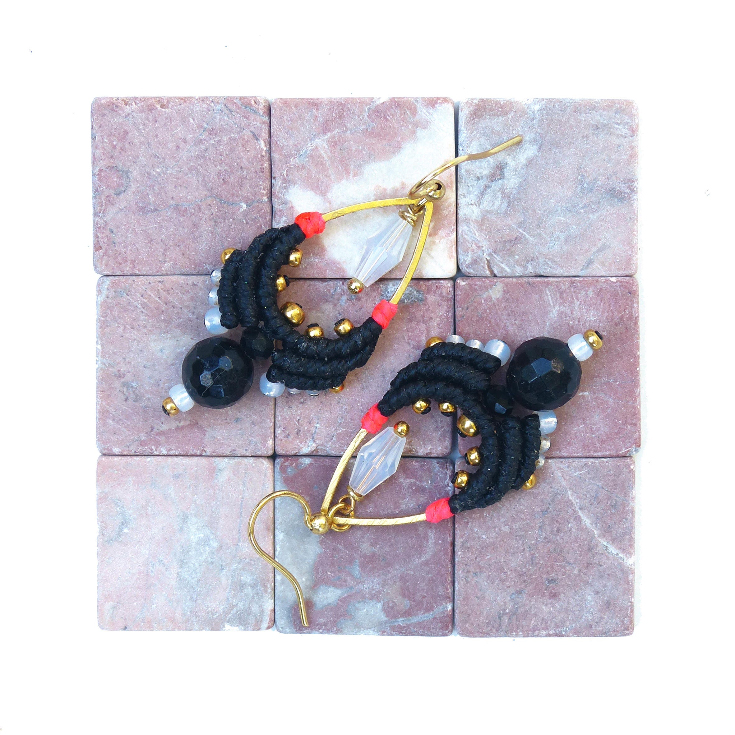 Peut inclure: Une paire de boucles d'oreilles noires et dorées en forme de larme. Les boucles d'oreilles sont faites de fil noir, de perles dorées et de cristaux transparents. Les boucles d'oreilles sont suspendues à des crochets dorés.