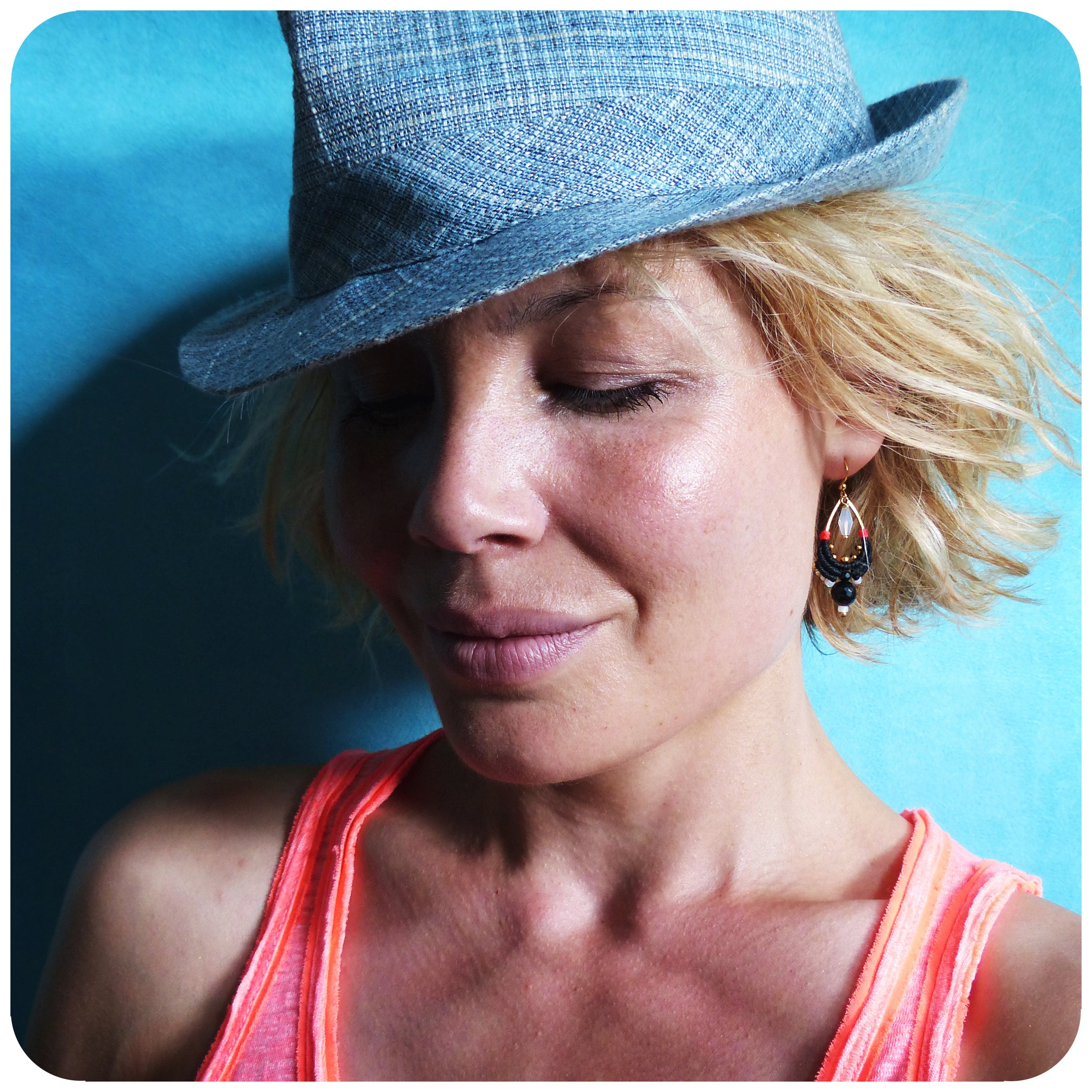 Peut inclure: Une femme aux cheveux blonds portant un chapeau en jean bleu et un débardeur corail. Elle porte des boucles d'oreilles pendantes avec des perles noires, blanches et rouges.
