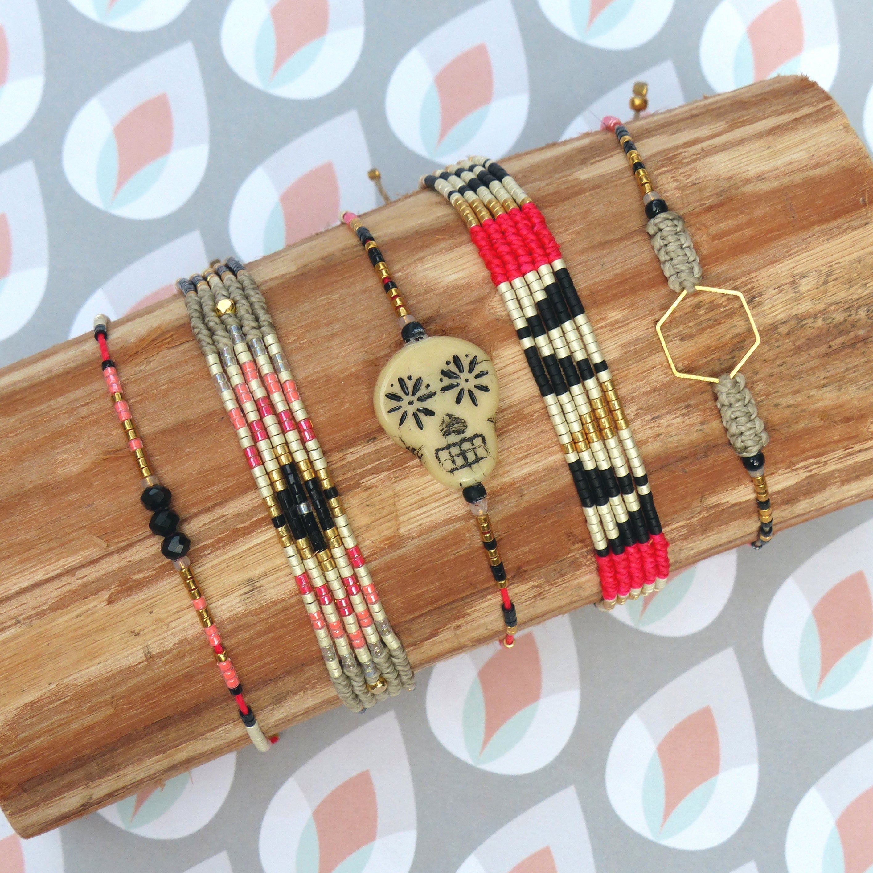 Peut inclure: Plusieurs bracelets faits à la main avec des motifs variés. Les bracelets sont ornés de perles noires, rouges, dorées et beiges. Un bracelet est orné d'un motif de crâne. Les bracelets sont présentés sur une surface en bois.