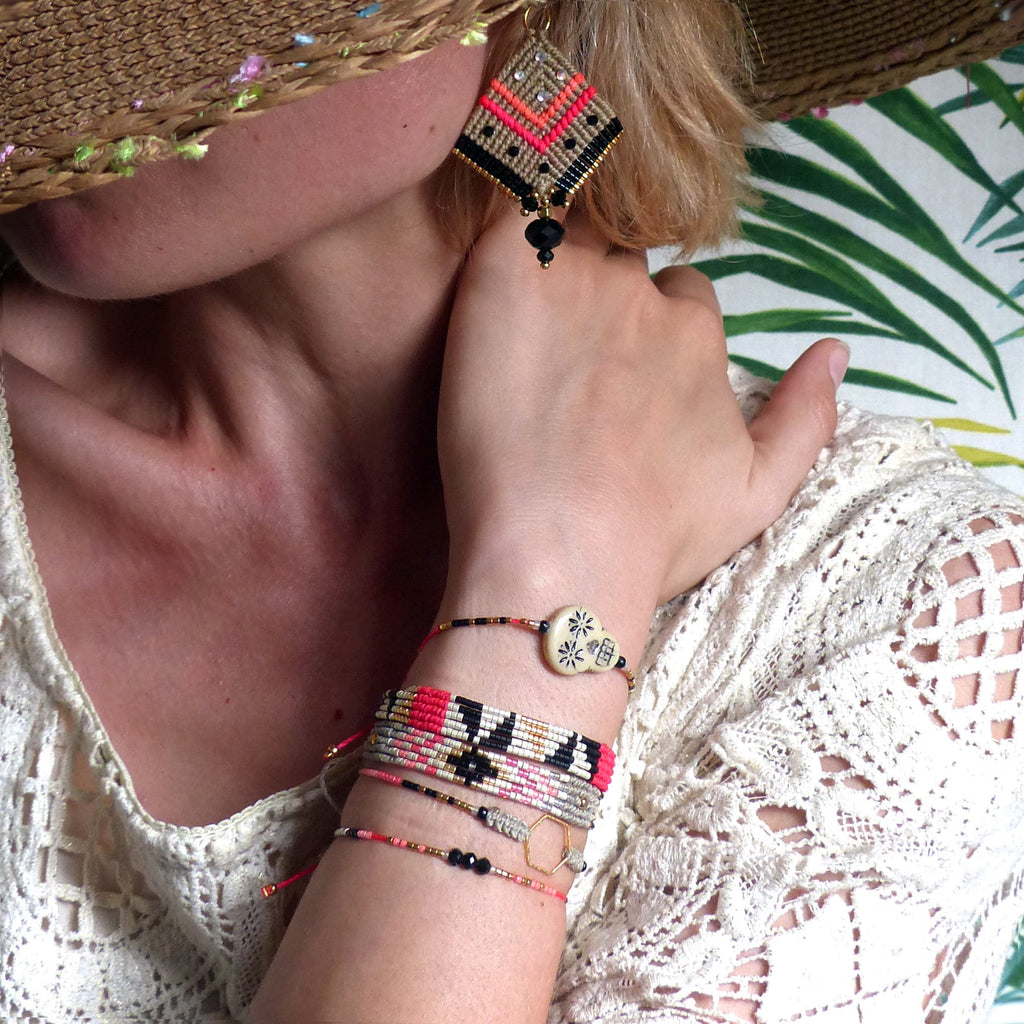 Peut inclure: Ensemble de bijoux faits à la main, comprenant une boucle d'oreille en forme de losange avec des accents noirs, corail et dorés, et plusieurs bracelets de perles. Les bracelets présentent diverses couleurs et motifs, avec une pièce maîtresse en forme de crâne.