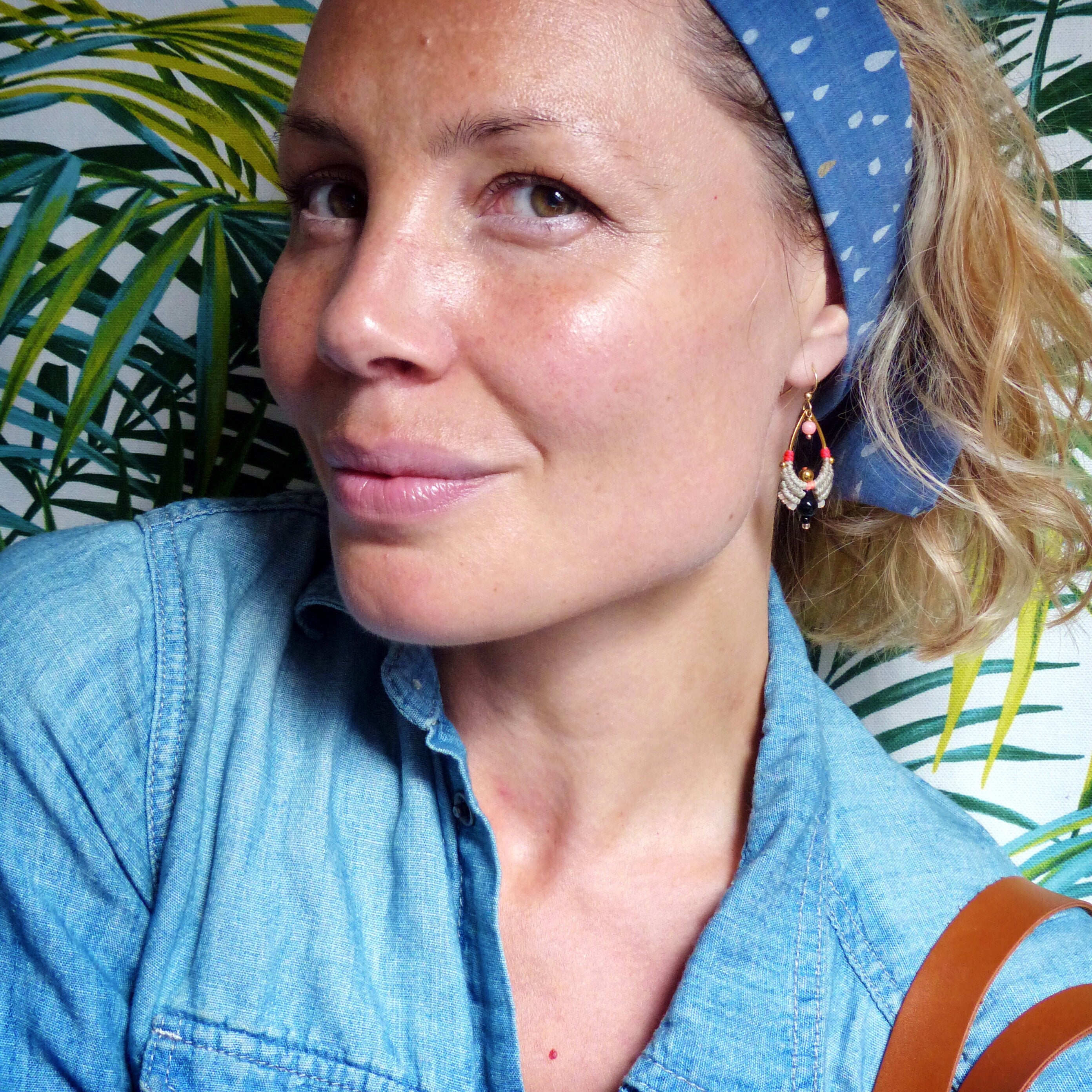 Peut inclure: Une femme portant une chemise en jean bleu avec un bandeau à motifs bleu et blanc. Elle porte des boucles d'oreilles dorées avec des perles noires, blanches et rouges.