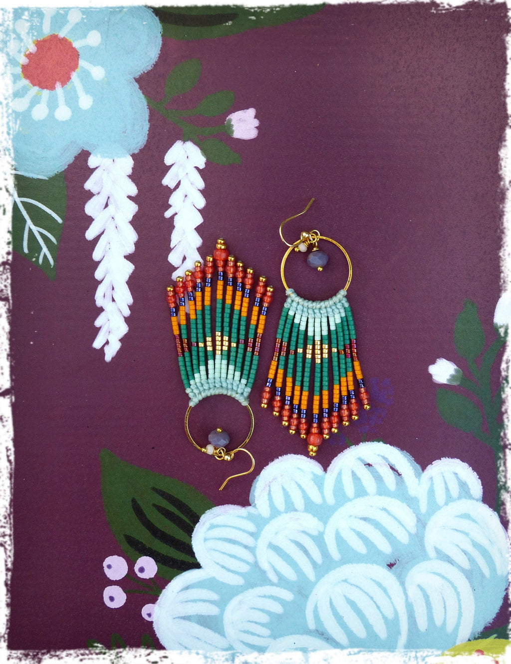 Peut inclure: Une paire de longues boucles d'oreilles en perles avec un anneau en or et une petite pierre ronde violette. Les boucles d'oreilles sont faites de perles vertes, orange et bleues et ont un design en frange.