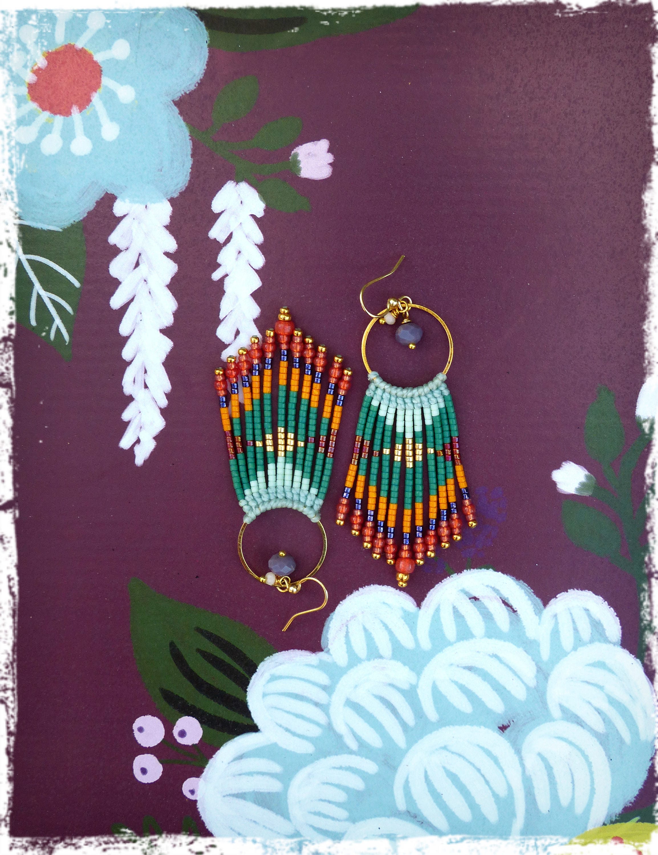 Peut inclure: Une paire de longues boucles d'oreilles en perles avec un anneau en or et une petite pierre ronde violette. Les boucles d'oreilles sont faites de perles vertes, orange et bleues et ont un design en frange.