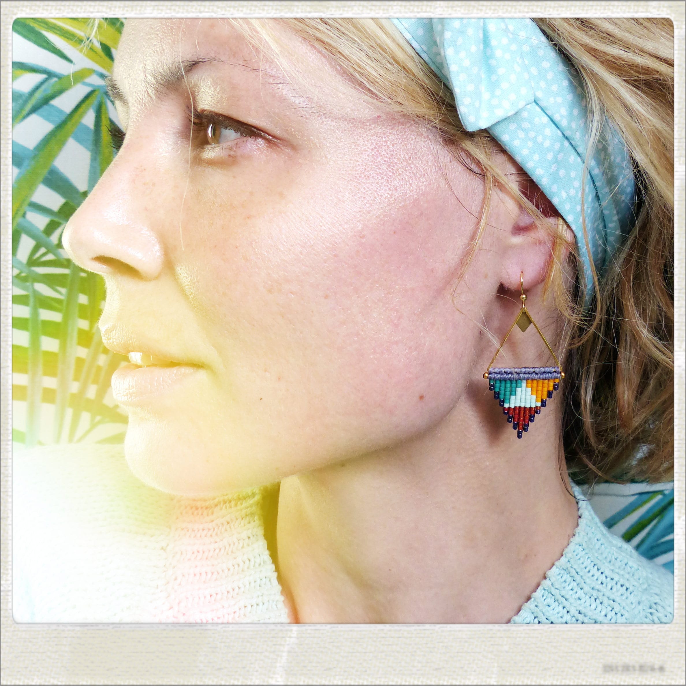 Peut inclure: Une femme portant un bandeau bleu clair à pois blancs et une paire de boucles d'oreilles triangulaires géométriques colorées. Les boucles d'oreilles sont faites de petites perles dans des tons de bleu, vert, orange et blanc.