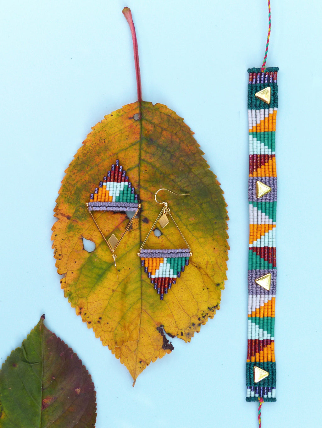 Peut inclure: Une paire de boucles d'oreilles triangulaires et un bracelet en perles colorées. Les boucles d'oreilles et le bracelet présentent un motif géométrique avec des perles vertes, orange, violettes et blanches. Les boucles d'oreilles ont des crochets dorés et le bracelet a un fermoir doré.