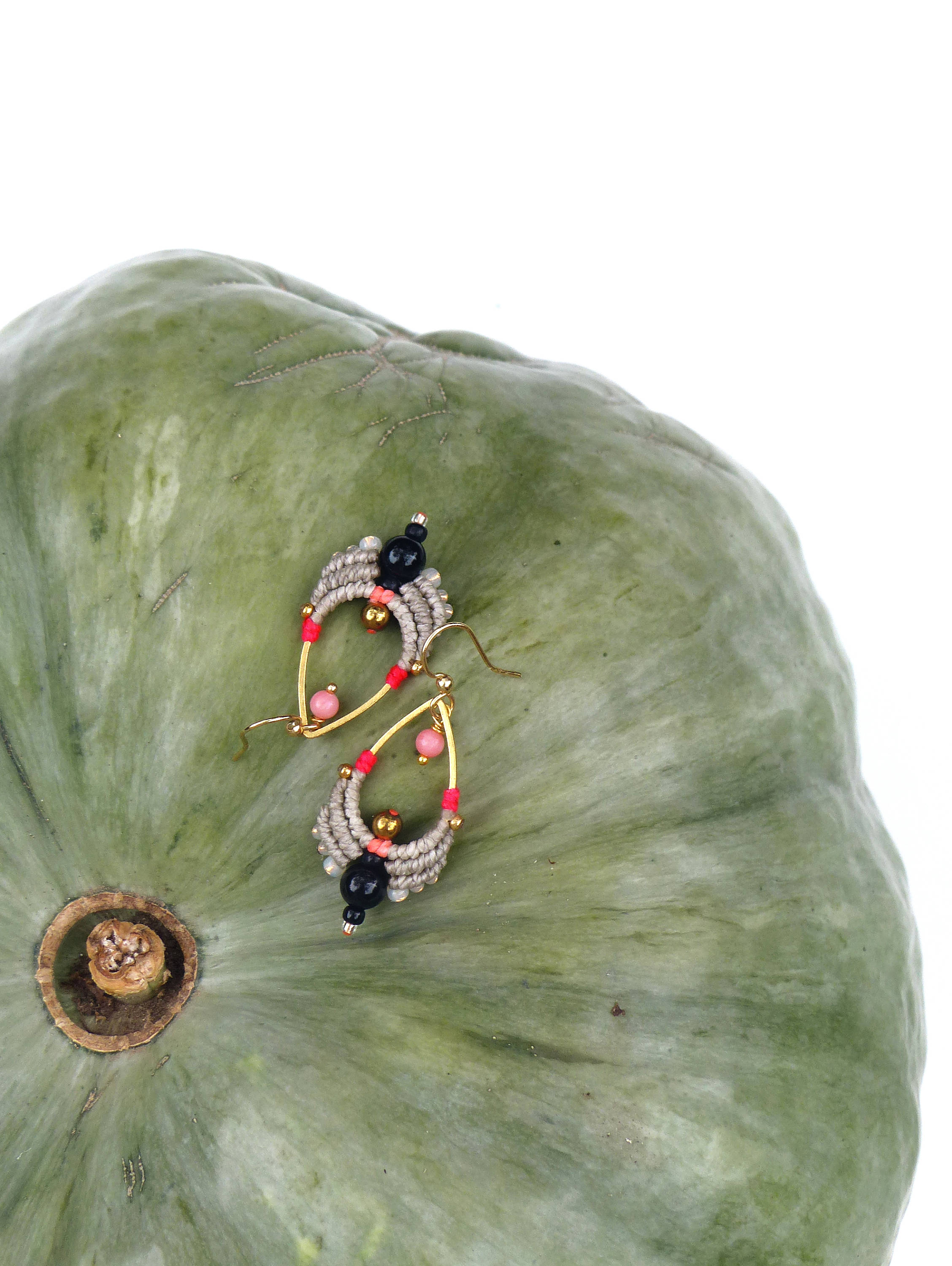 Peut inclure: Une paire de boucles d'oreilles faites à la main en forme de larme. Les boucles d'oreilles sont faites avec de la ficelle grise, des perles noires et roses et des accents dorés.