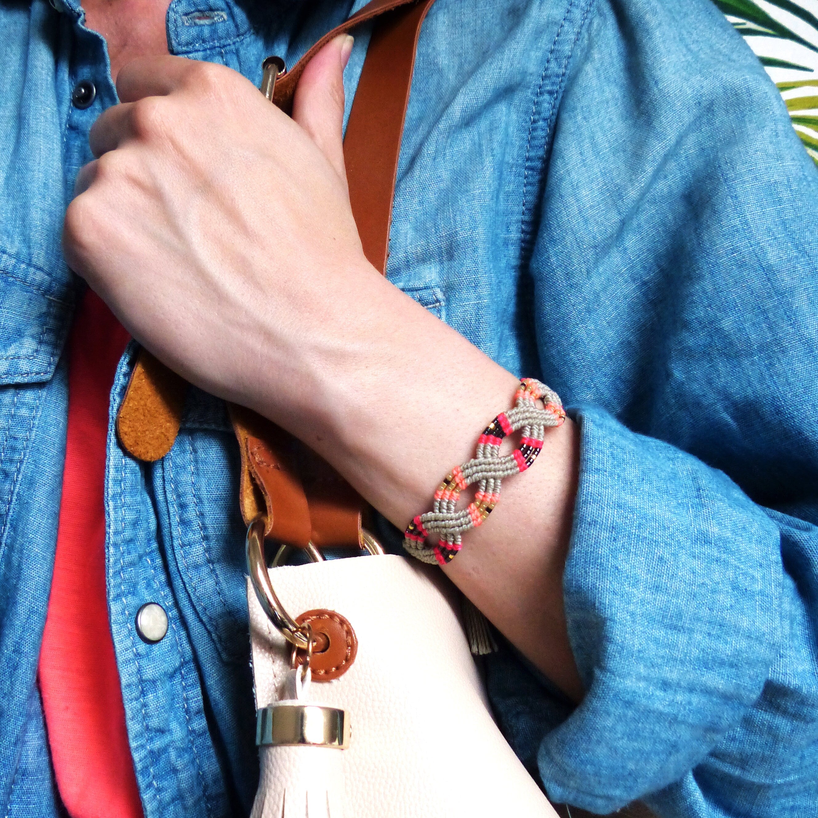 Peut inclure: Un bracelet tressé gris, rose et noir avec un motif tissé. Le bracelet est porté au poignet.