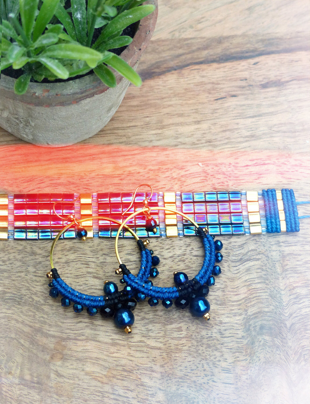 Peut inclure: Une paire de boucles d'oreilles créoles en perles bleues et noires avec des accents dorés. Les boucles d'oreilles sont faites de petites perles rondes et ont un charme suspendu en bas.