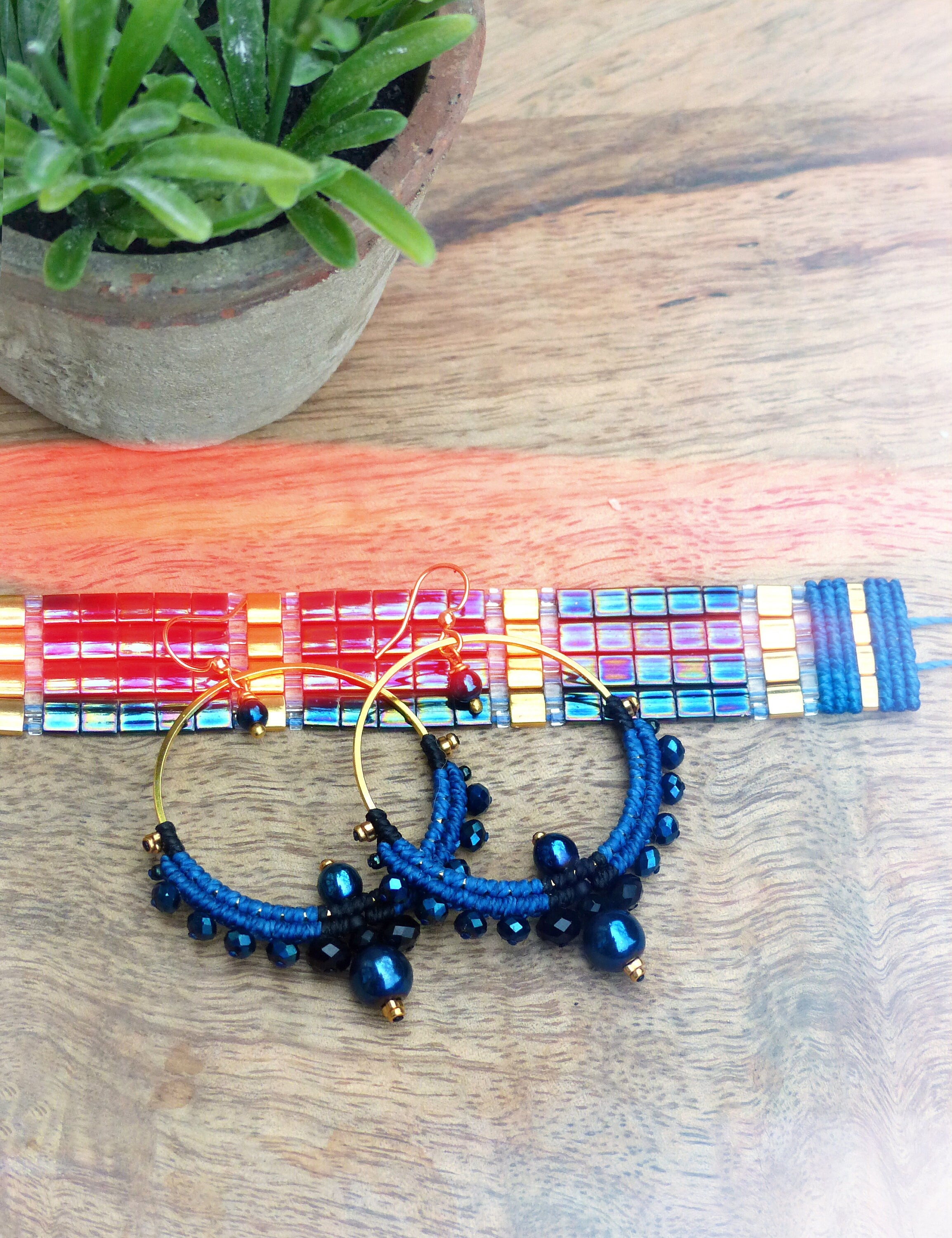 Peut inclure: Une paire de boucles d'oreilles créoles en perles bleues et noires avec des accents dorés. Les boucles d'oreilles sont faites de petites perles rondes et ont un charme suspendu en bas.