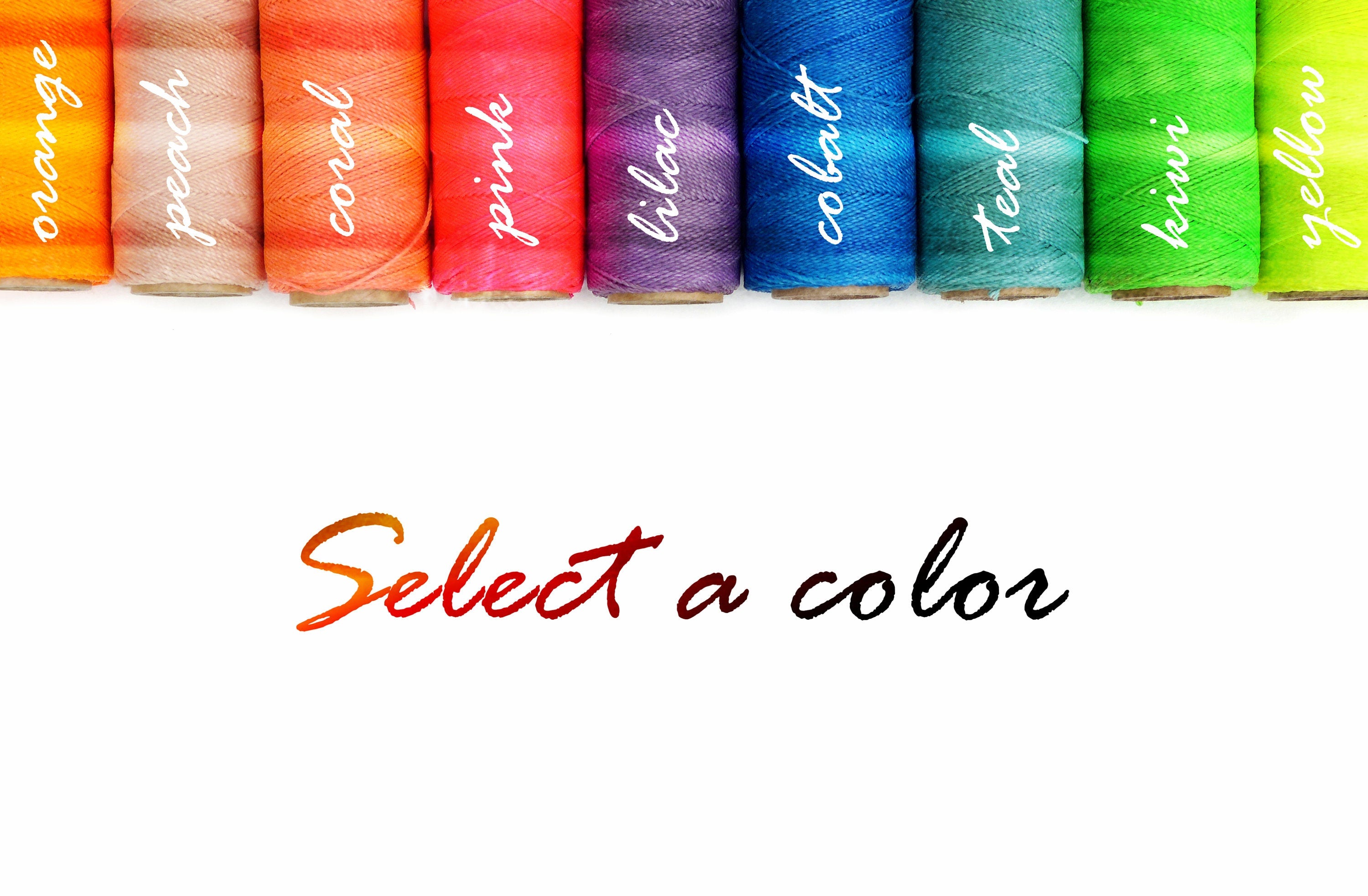 Peut inclure: Dix bobines de fil de différentes couleurs, dont orange, pêche, corail, rose, lilas, cobalt, sarcelle, kiwi et jaune. Les bobines sont disposées en arc-en-ciel. Le texte "Sélectionnez une couleur" est écrit sous les bobines.