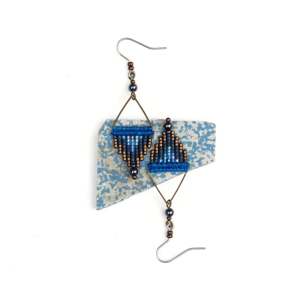 Peut inclure: Une paire de boucles d'oreilles en perles bleues et brunes de forme triangulaire. Les boucles d'oreilles sont suspendues à un morceau de carrelage en céramique à motifs bleus et blancs.