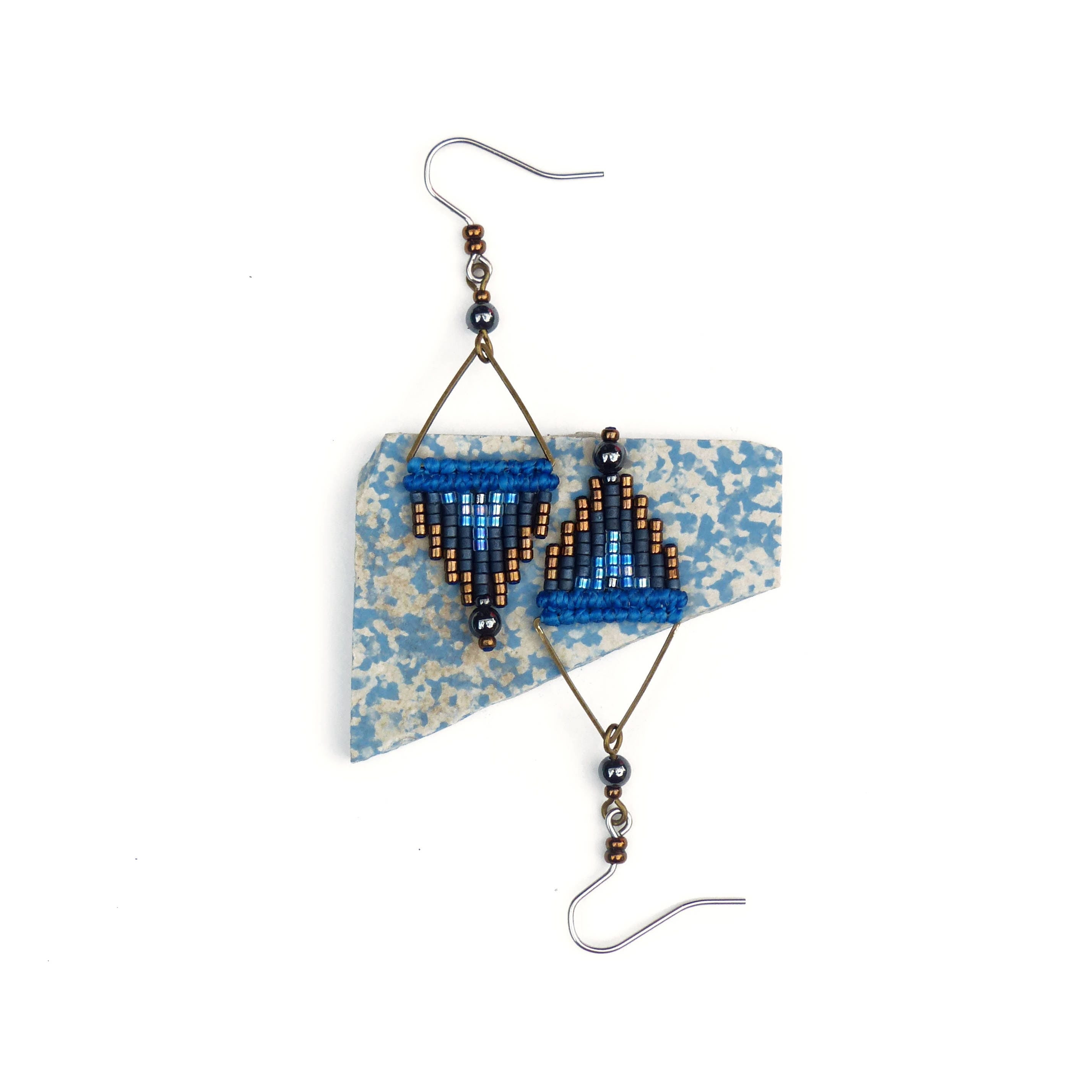 Peut inclure: Une paire de boucles d'oreilles en perles bleues et brunes de forme triangulaire. Les boucles d'oreilles sont suspendues à un morceau de carrelage en céramique à motifs bleus et blancs.