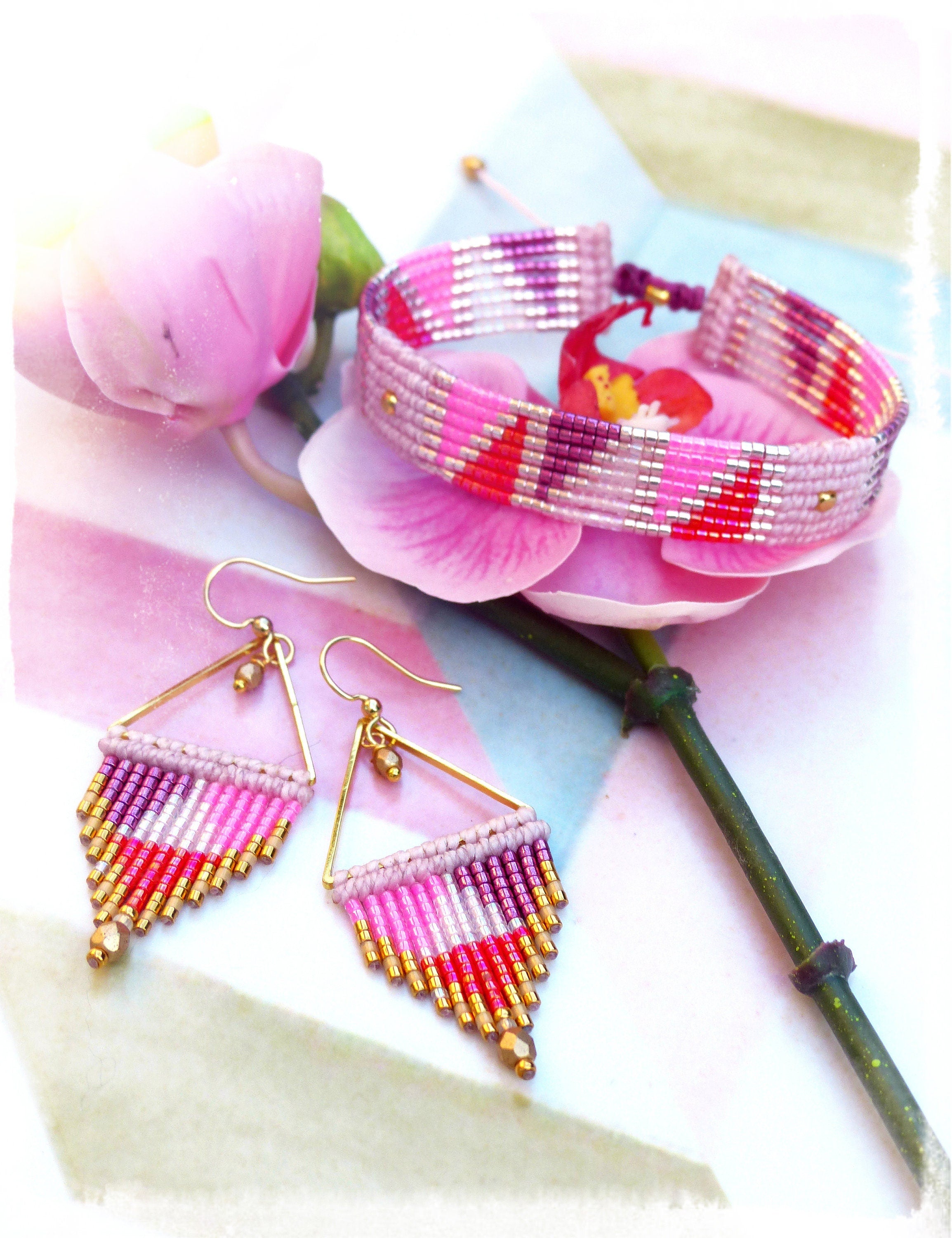 Peut inclure: Un ensemble de boucles d'oreilles et de bracelet en perles roses, rouges et dorées. Les boucles d'oreilles sont de forme triangulaire et pendantes. Le bracelet est une seule rangée de perles.