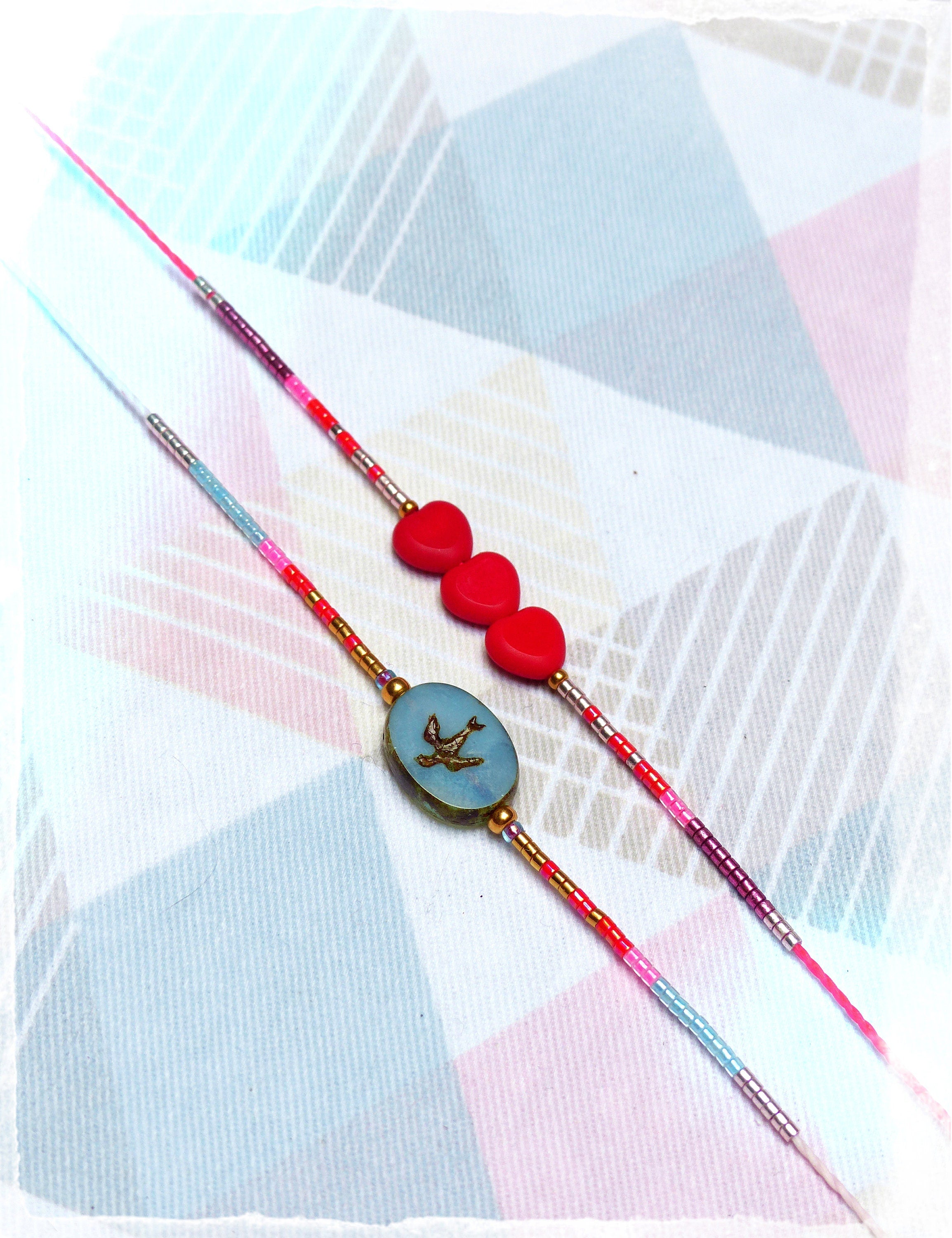 Peut inclure: Deux bracelets d'amitié avec des perles colorées, l'un avec des breloques en forme de cœur rouge et l'autre avec un charme ovale bleu orné d'un oiseau doré.