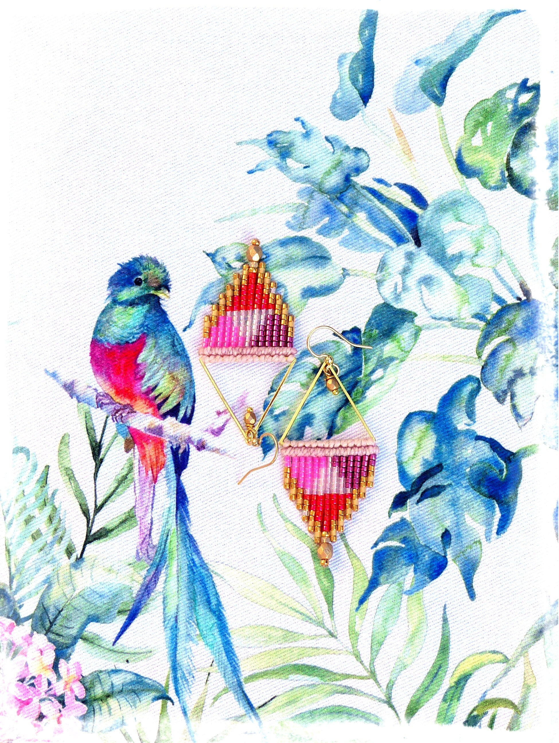 Peut inclure: Une paire de boucles d'oreilles triangulaires en perles roses, rouges et dorées. Les boucles d'oreilles sont suspendues à des crochets dorés et sont placées sur un fond de fleurs aquarellées bleues et vertes.
