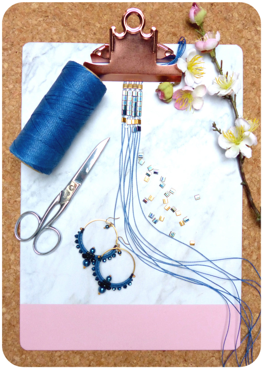 Peut inclure: Gros plan d'un bracelet en perles bleu et or avec une bobine de fil bleu, une paire de boucles d'oreilles créoles dorées avec des perles bleues et une paire de ciseaux argentés sur une surface en marbre blanc.