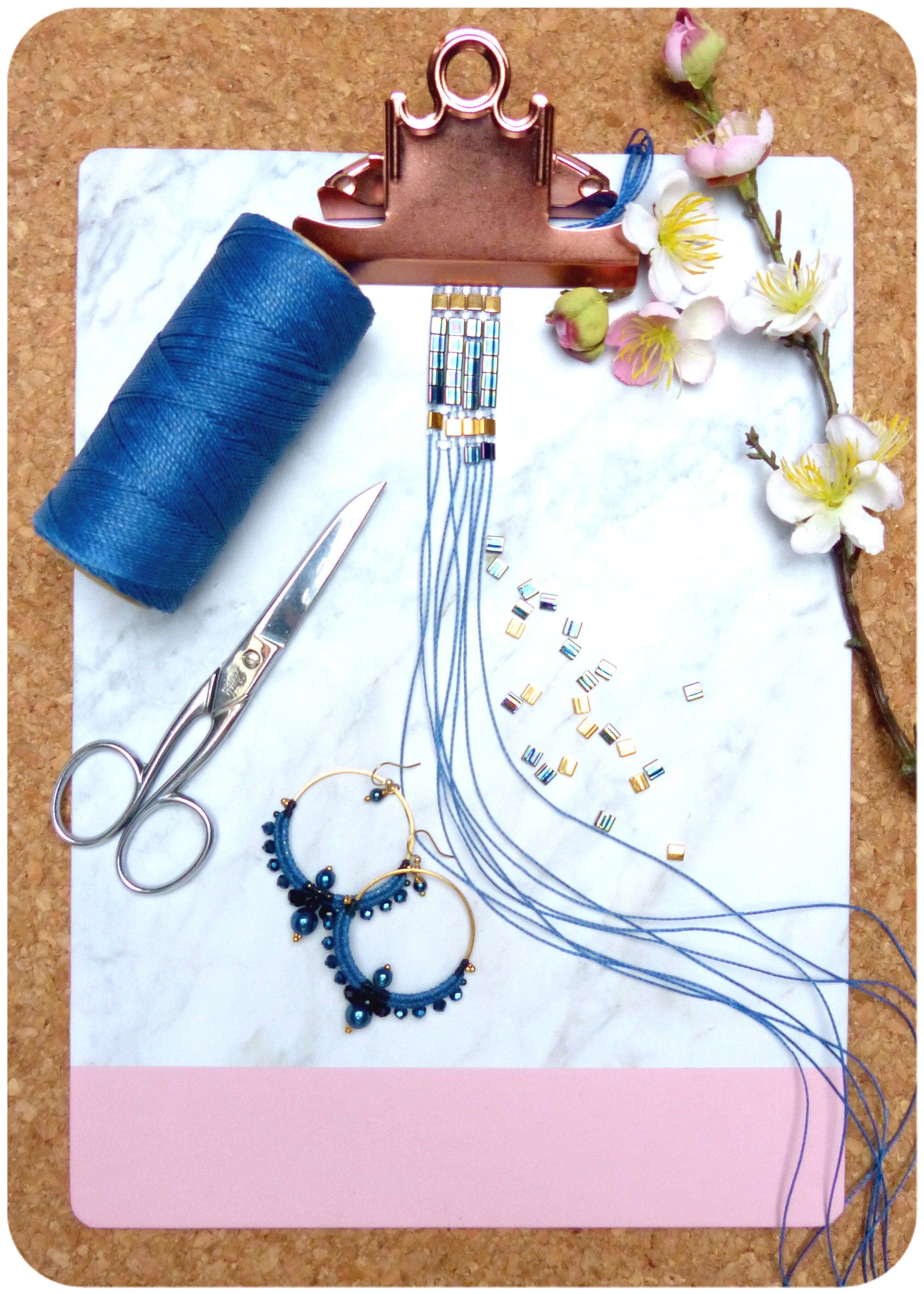 Peut inclure: Gros plan d'un bracelet en perles bleu et or avec une bobine de fil bleu, une paire de boucles d'oreilles créoles dorées avec des perles bleues et une paire de ciseaux argentés sur une surface en marbre blanc.