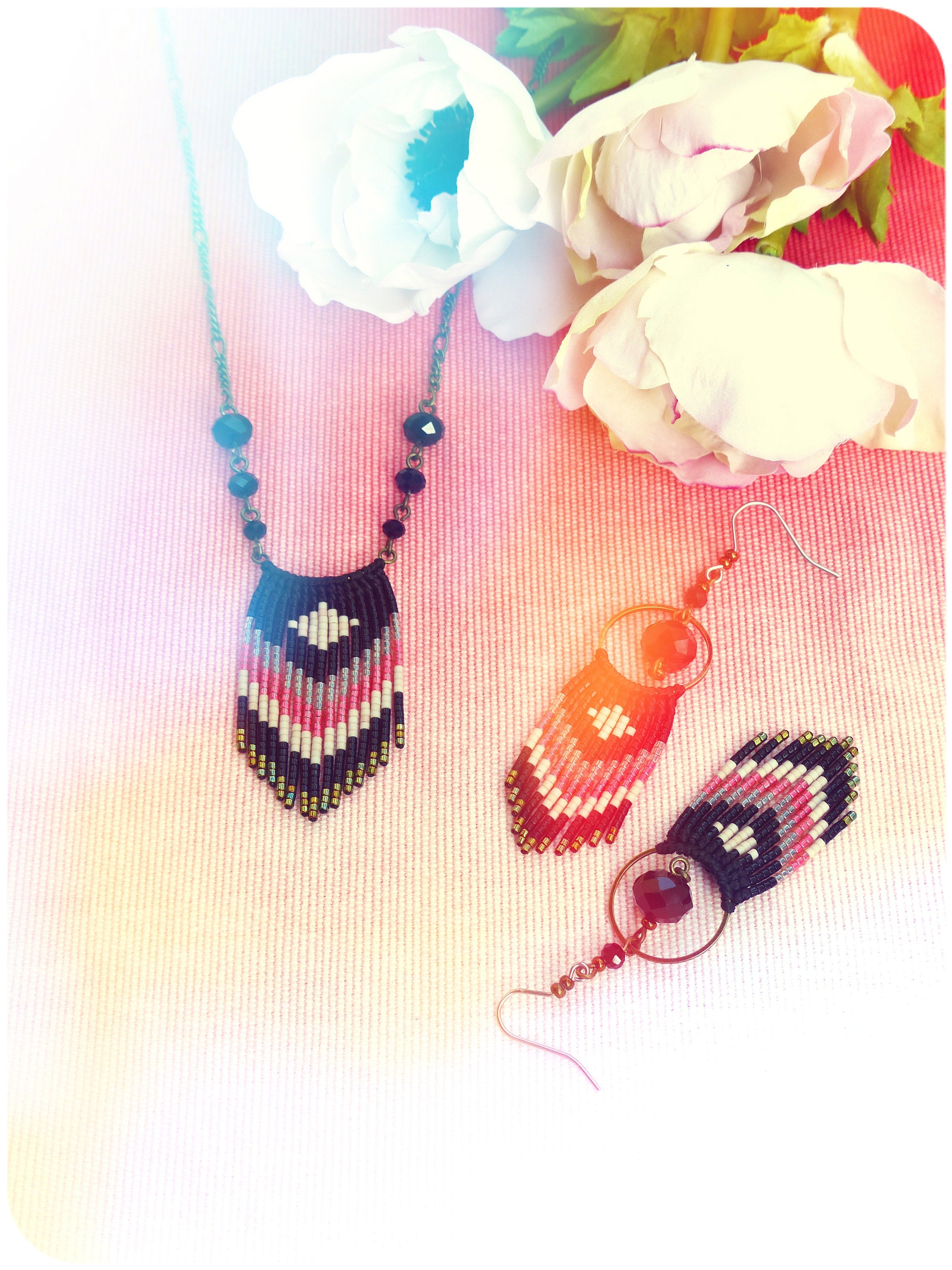 Peut inclure: Un ensemble de bijoux en perles comprenant un collier et des boucles d'oreilles. Le collier a une chaîne noire avec des perles noires et un pendentif en perles avec un motif géométrique en noir, blanc, rose et gris. Les boucles d'oreilles ont un motif géométrique similaire en noir, blanc, rose et gris avec un accent de pierre précieuse rouge.