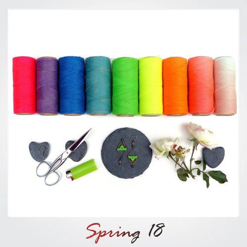 Peut inclure: Un assortiment arc-en-ciel de bobines de fil colorées, une paire de boucles d'oreilles en perles vertes et noires, une paire de ciseaux, un briquet et deux pierres grises en forme de cœur. Le texte "Spring 18" est écrit en rouge en bas de l'image.