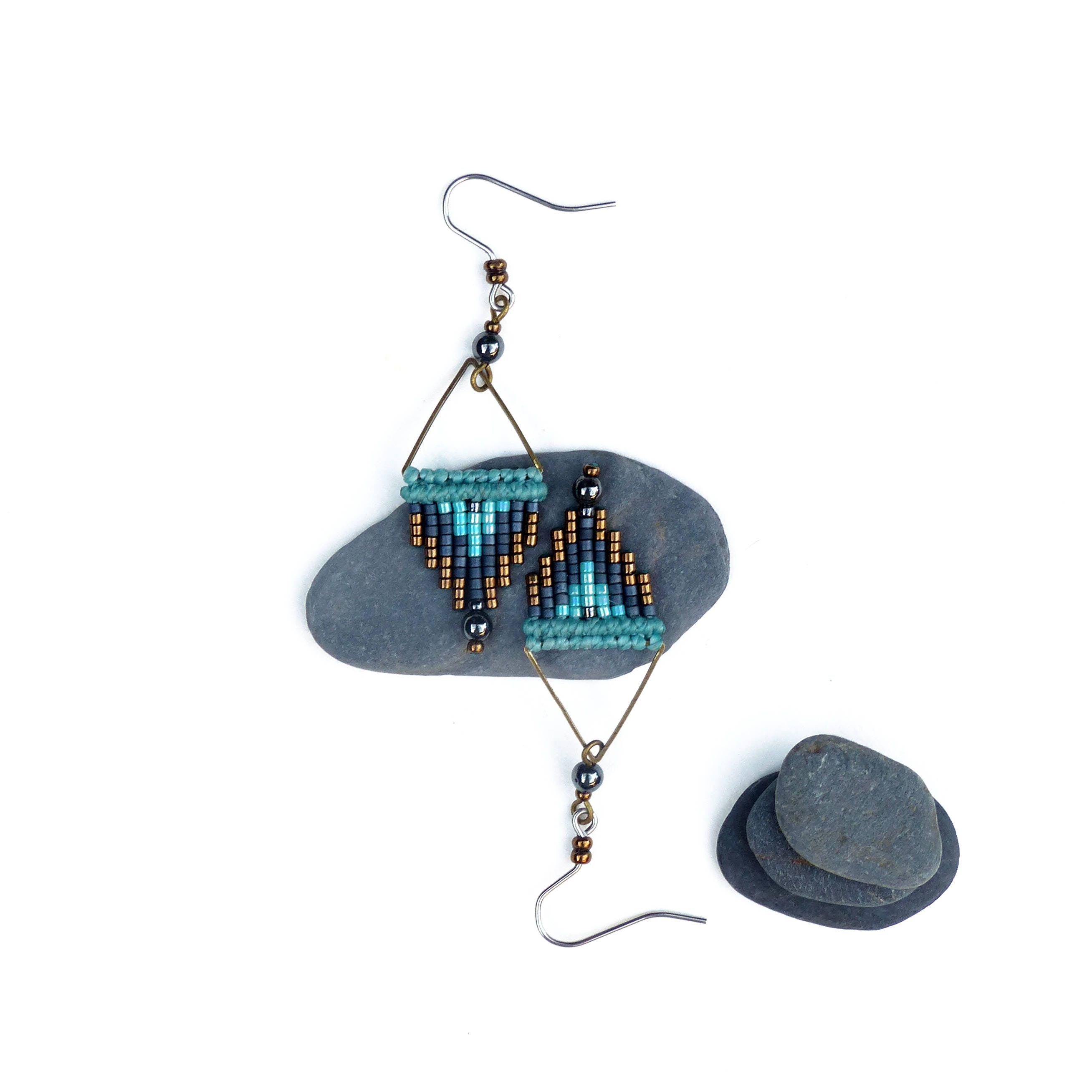 Peut inclure: Une paire de boucles d'oreilles en perles turquoise et noires avec des accents dorés suspendues à une pierre grise. Les boucles d'oreilles ont la forme d'un triangle.