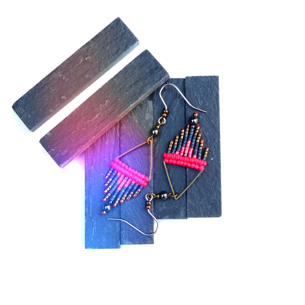 Peut inclure: Une paire de boucles d'oreilles faites à la main avec un design géométrique. Les boucles d'oreilles sont faites de perles noires, rouges et dorées et ont une forme triangulaire. Les boucles d'oreilles sont suspendues à un fil d'or.