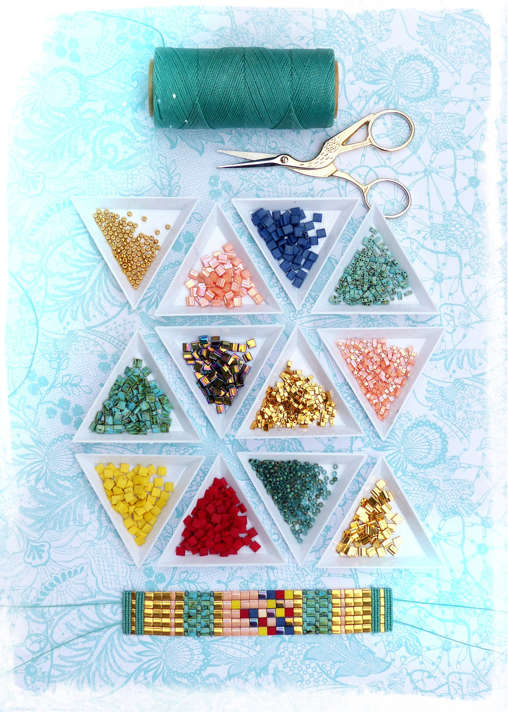 Peut inclure: Composition de fournitures de bricolage avec une bobine de fil vert d'eau, des ciseaux dorés et des plateaux triangulaires remplis de perles colorées. Un bracelet de perles avec des perles dorées, turquoise, roses et bleues est en bas. Fond bleu clair à motifs floraux.