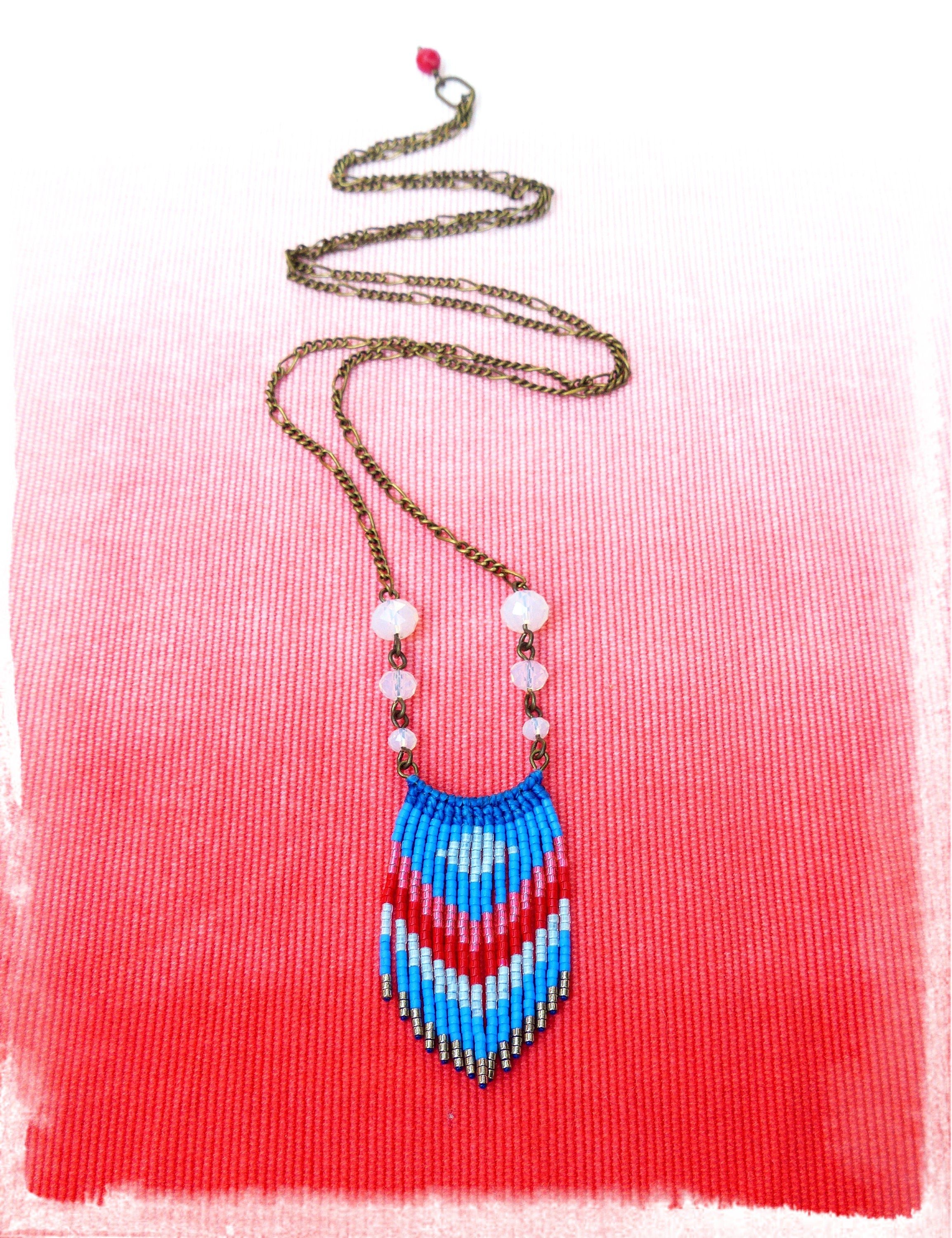 Peut inclure: Un long collier avec une chaîne en bronze et un pendentif composé de perles bleues, rouges et blanches. Le pendentif présente un motif géométrique. Le collier comporte également de petites perles blanches rondes et une petite perle rouge en haut de la chaîne.