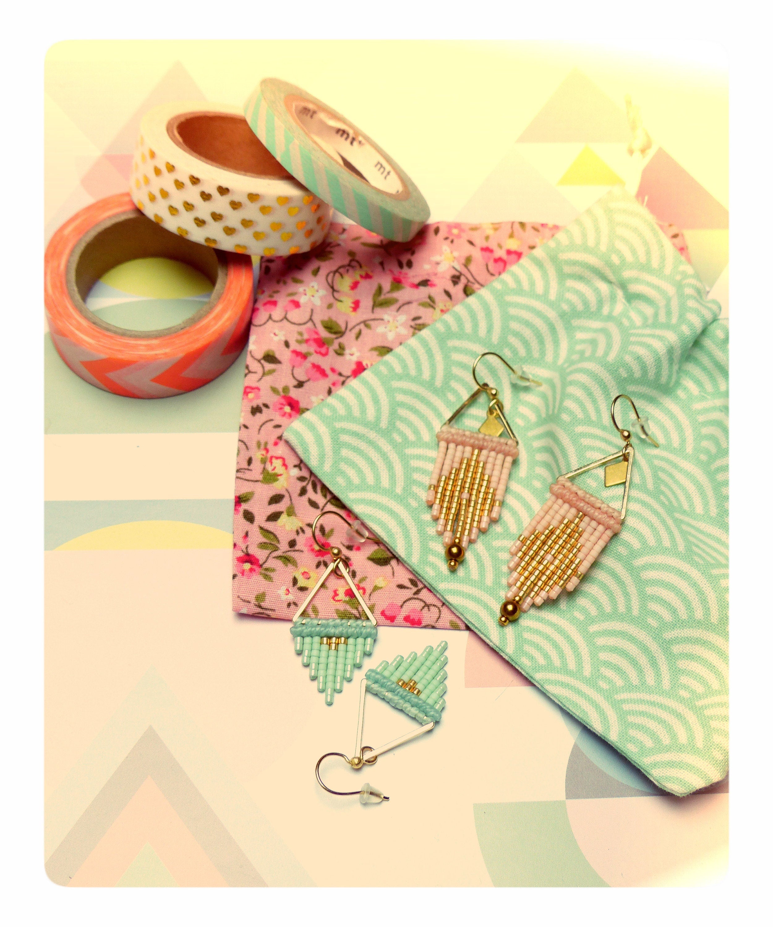 Peut inclure: Une paire de boucles d'oreilles délicates avec des accents dorés et des perles roses et bleues. Les boucles d'oreilles sont présentées sur une pochette en tissu avec un motif floral et un motif de vagues.