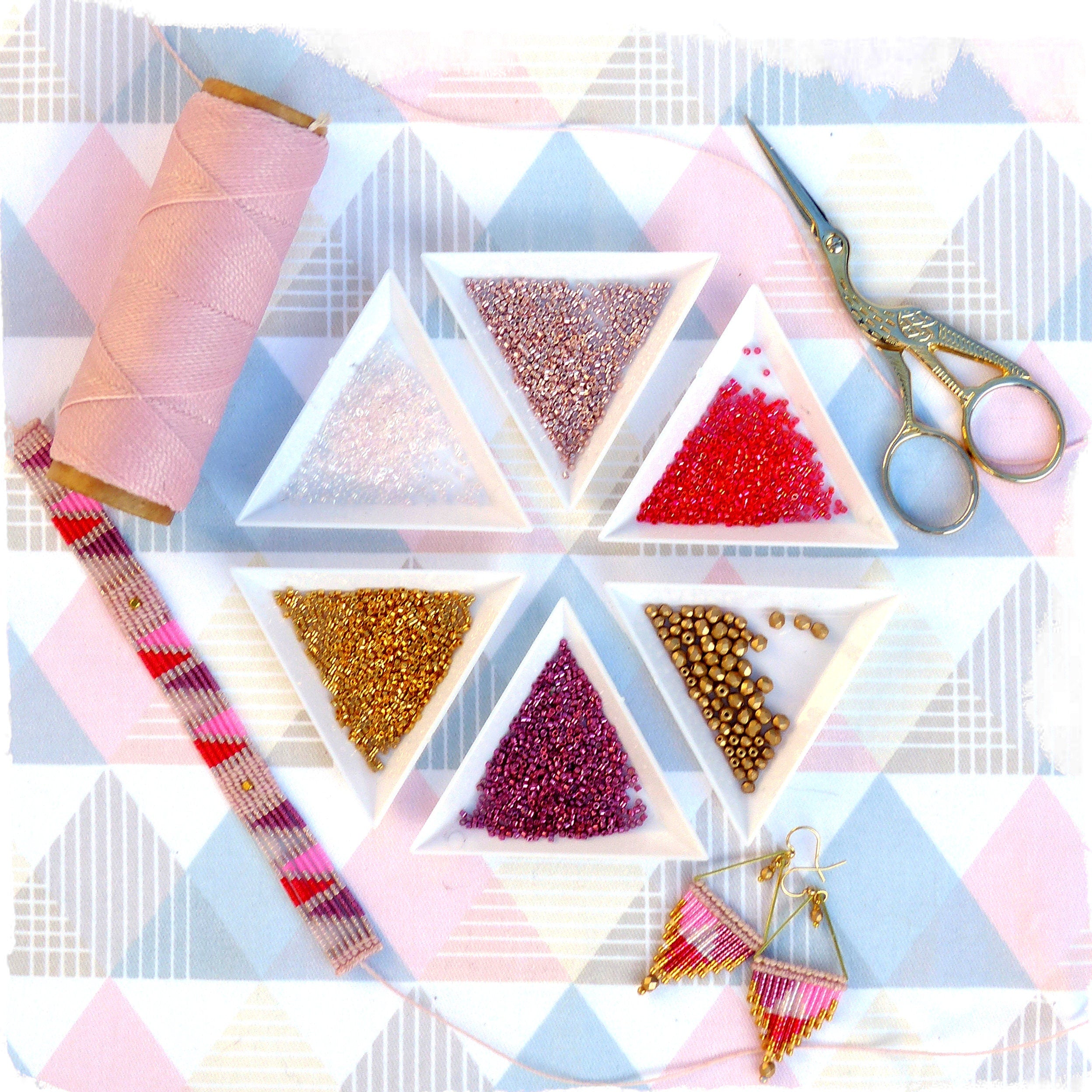 Peut inclure: Un ensemble de sept coupelles triangulaires remplies de perles de différentes couleurs, dont de l'or, du rose, du rouge, du blanc et de l'or rose. Une bobine de fil rose, une paire de ciseaux dorés et une paire de boucles d'oreilles roses et dorées sont également inclus.