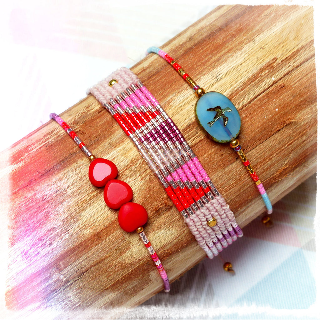 Peut inclure: Trois bracelets avec des perles et des breloques colorées. Un bracelet a un charme bleu avec un motif d'oiseau, un autre a trois perles en forme de cœur rouges et le troisième a un motif multicolore de perles roses, rouges, blanches et dorées.