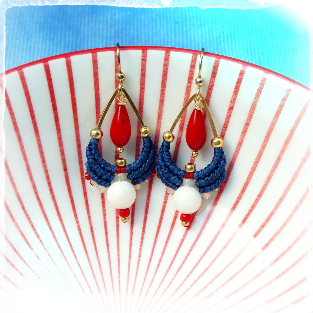 Peut inclure: Une paire de boucles d'oreilles pendantes avec un motif rouge, blanc et bleu. Les boucles d'oreilles présentent un pendentif en forme de larme de couleur dorée avec une perle rouge, un motif macramé bleu et blanc et une perle blanche.