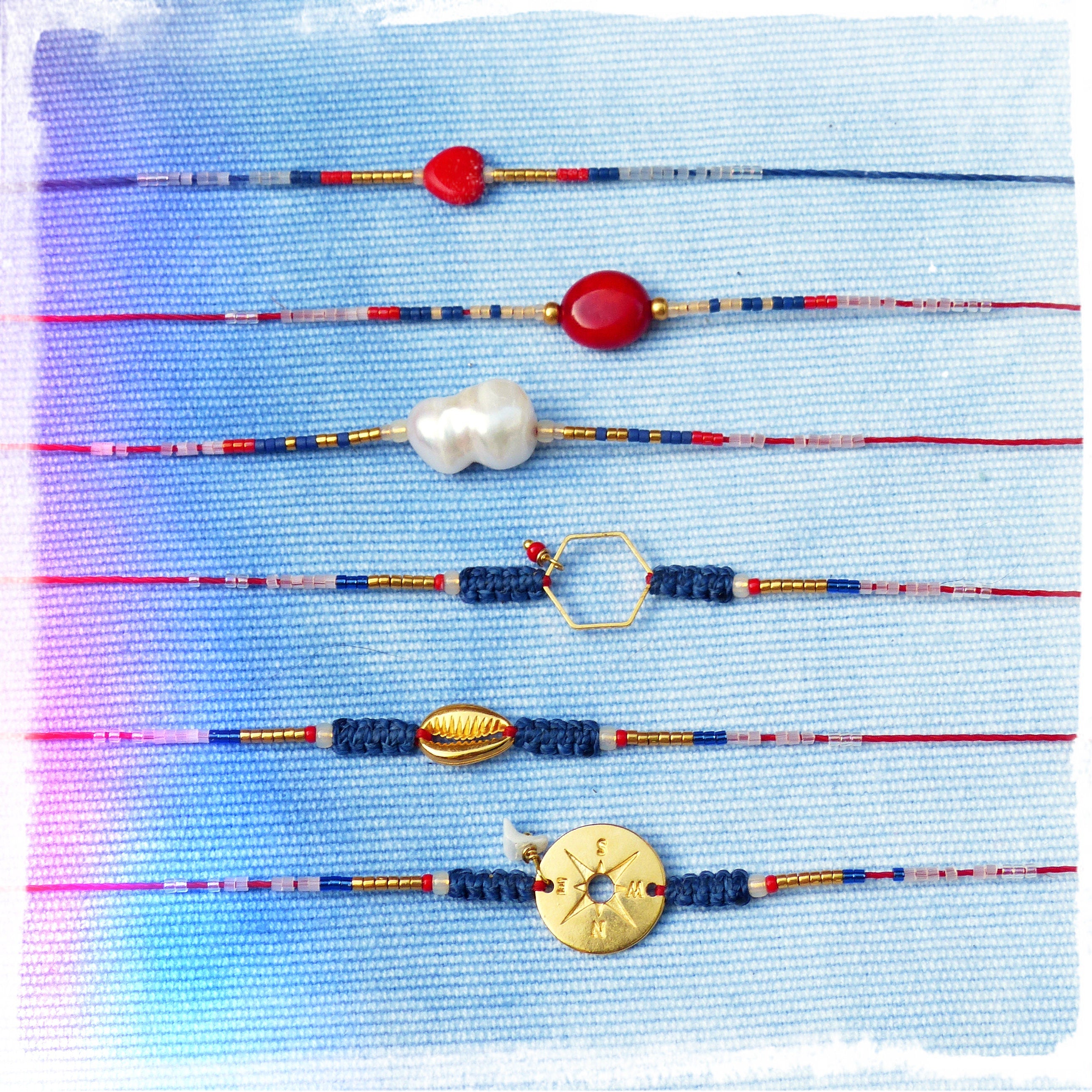 Peut inclure: Six bracelets colorés avec différents pendentifs, dont un cœur rouge, un ovale rouge, une perle blanche, un hexagone doré, un coquillage et une boussole dorée. Les bracelets sont faits de perles bleues, rouges et dorées sur un fond blanc.