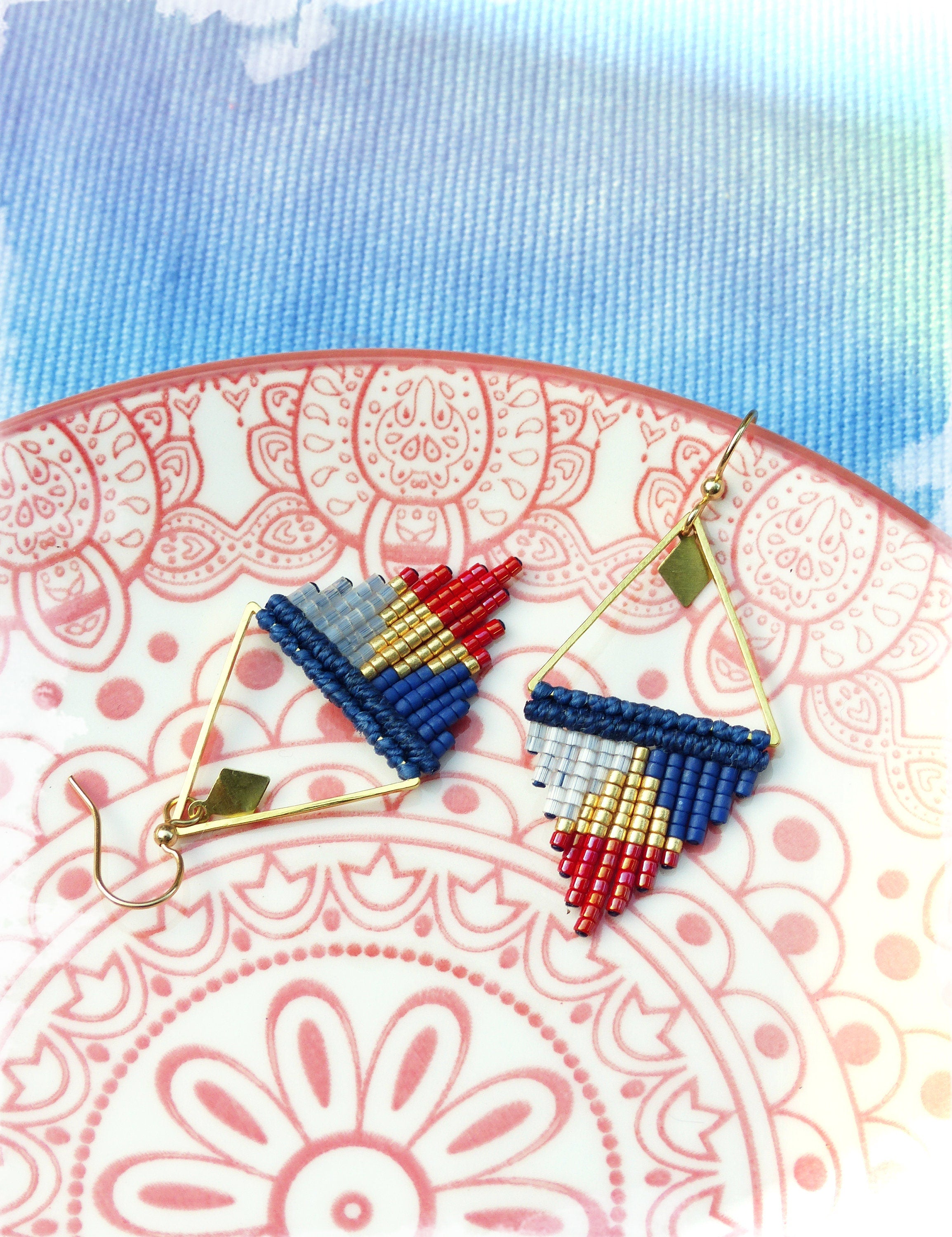 Peut inclure: Une paire de boucles d'oreilles triangulaires avec un fil doré et des perles bleues, rouges, blanches et dorées.